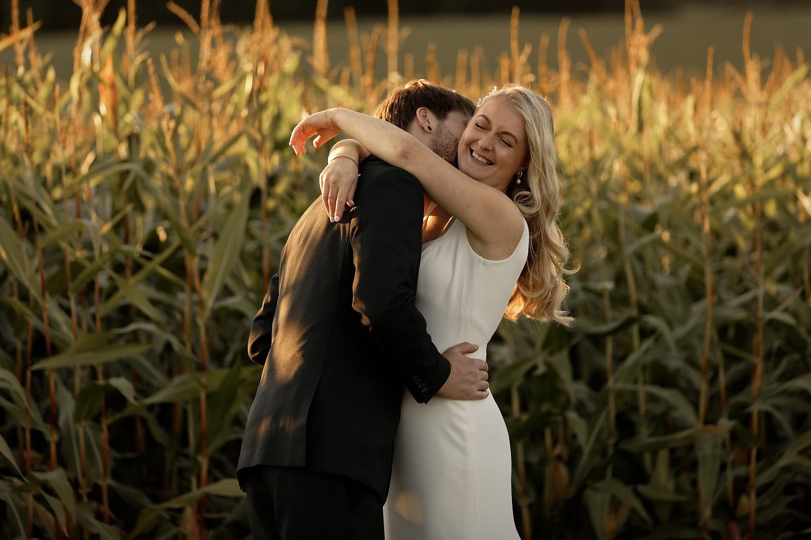 Bride laughing while embracing the groom in the cornfield at Fitzleroi Barn
