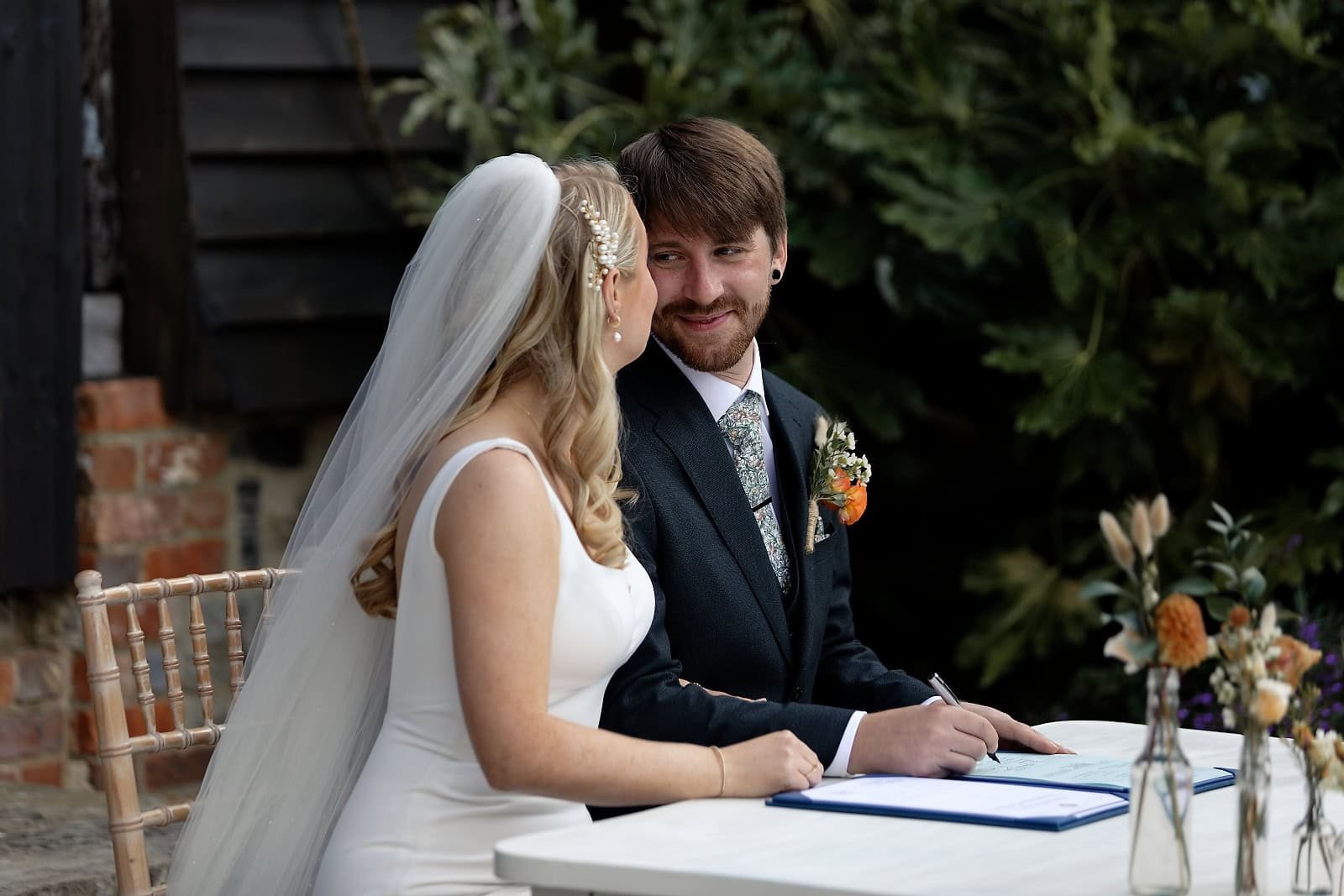 Bride and groom smiling while signing the register at their Fitzleroi Barn wedding