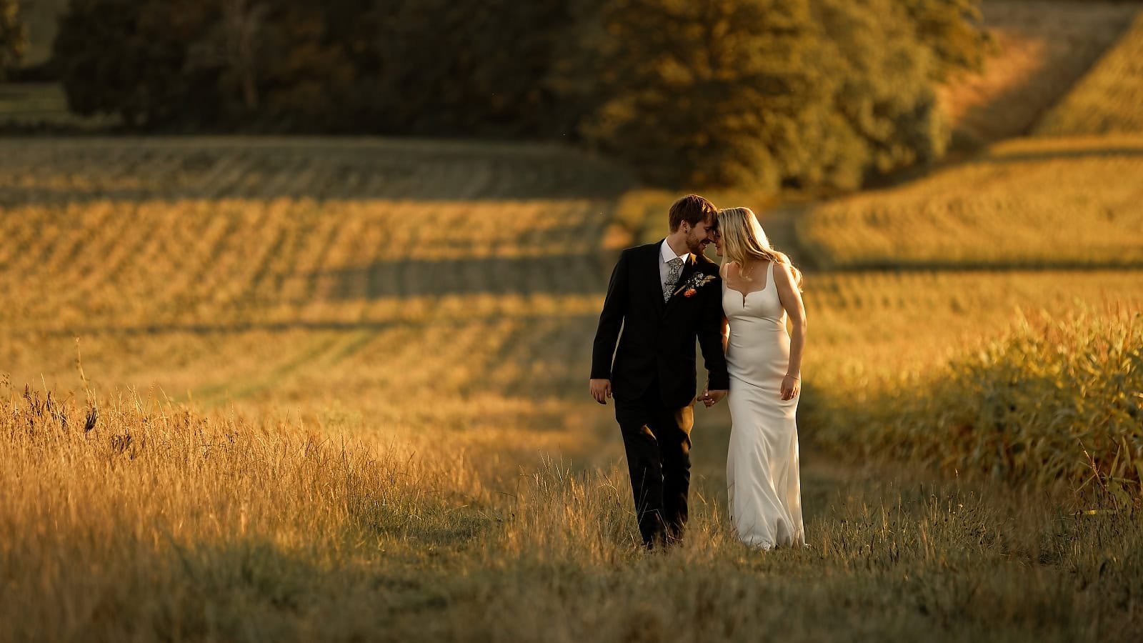 Newlyweds walking together through the fields at Fitzleroi Barn during golden hour
