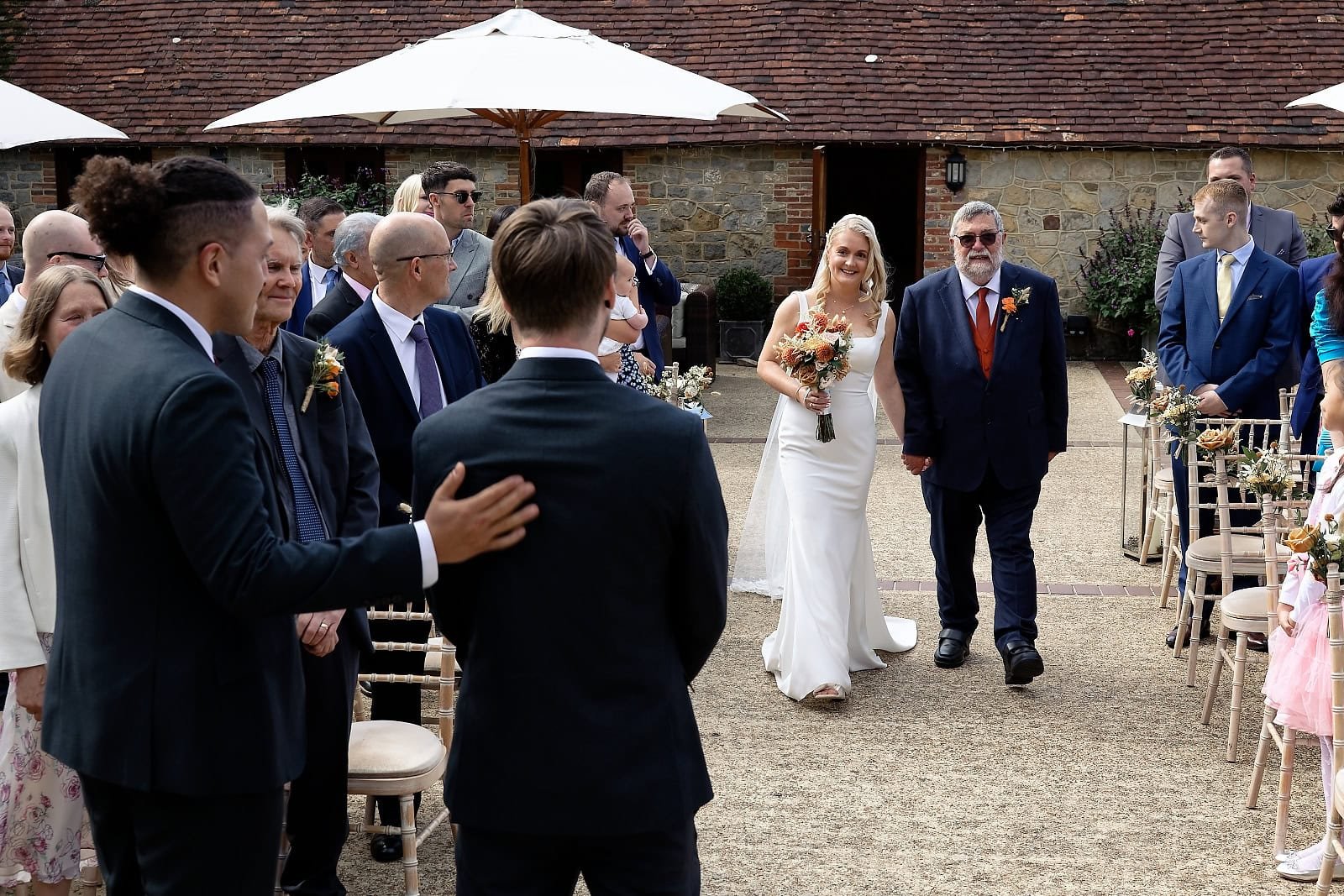 Fitzleroi Barn wedding photographer captures the bride walking into the courtyard with her father