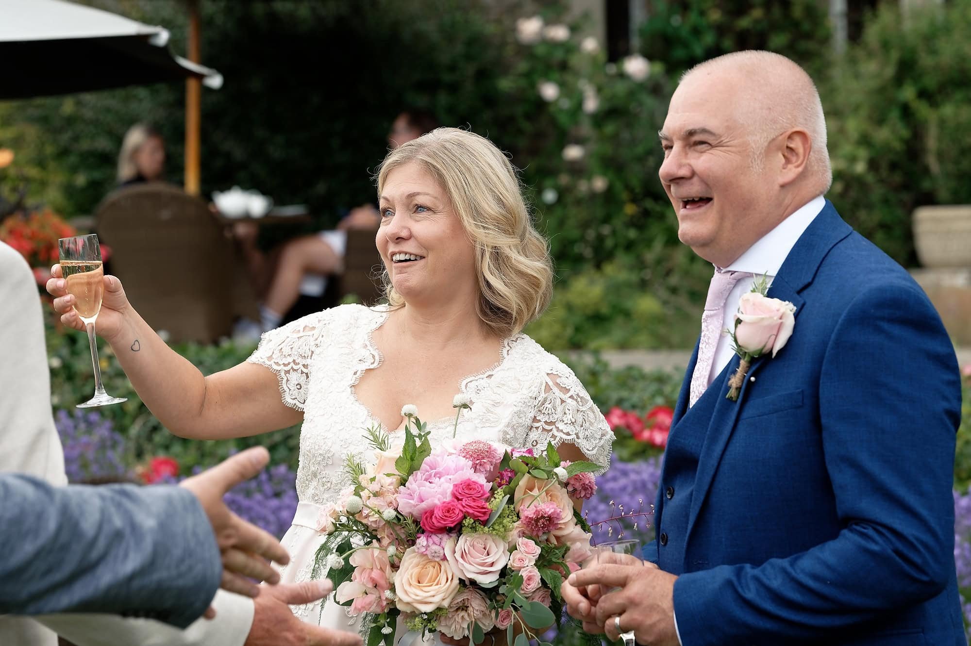 Bride and groom smiling and laughing with champagne glasses after their ceremony at South Lodge Hotel, Horsham