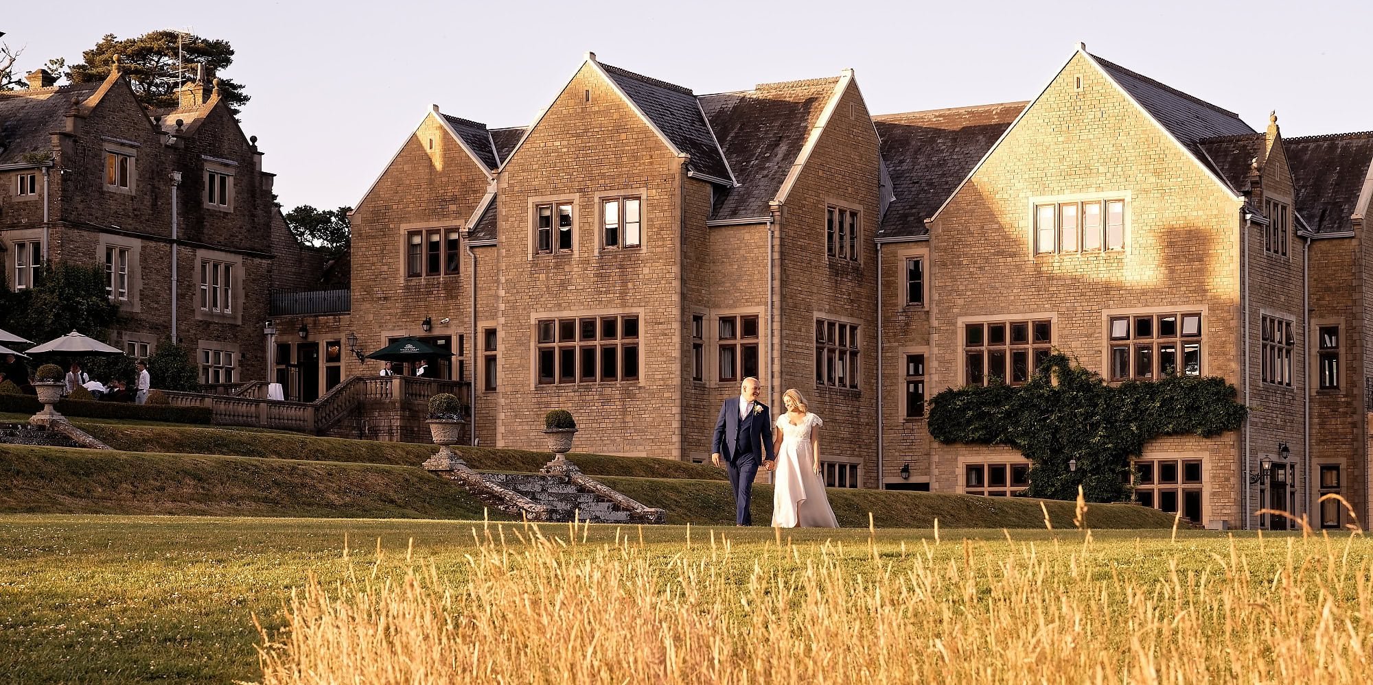 Bride and groom walking across the lawns at the rear of South Lodge Hotel during their couple portraits, Horsham