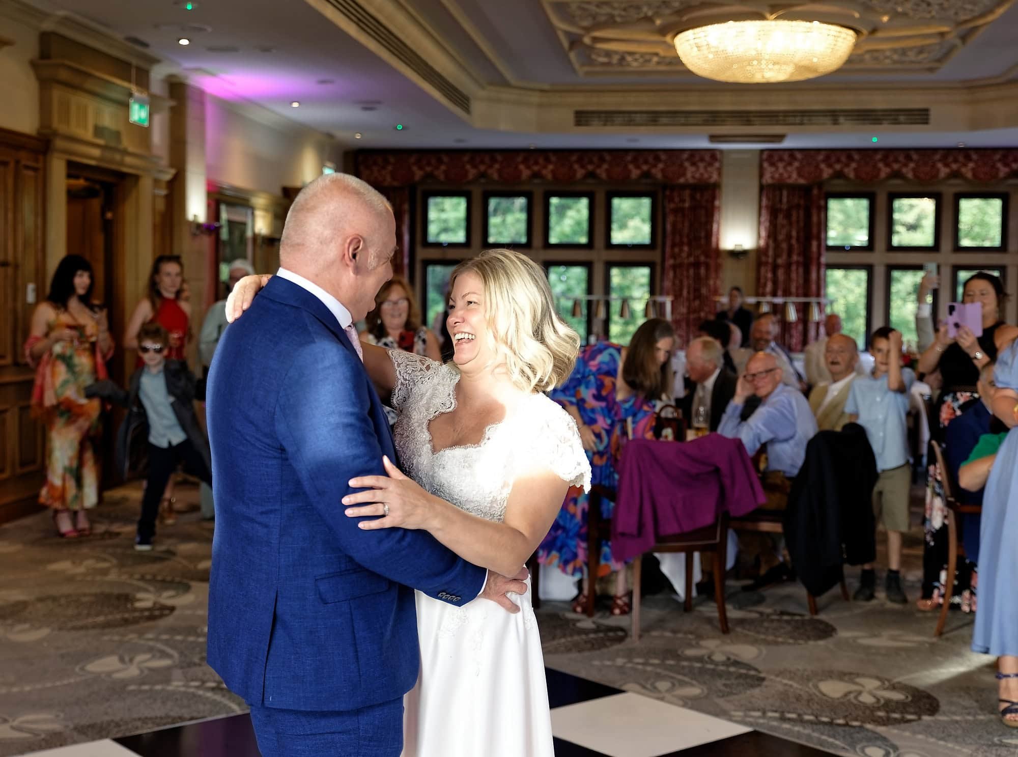 Bride and groom laughing during their first dance with guests looking on at South Lodge Hotel, Horsham, West Sussex