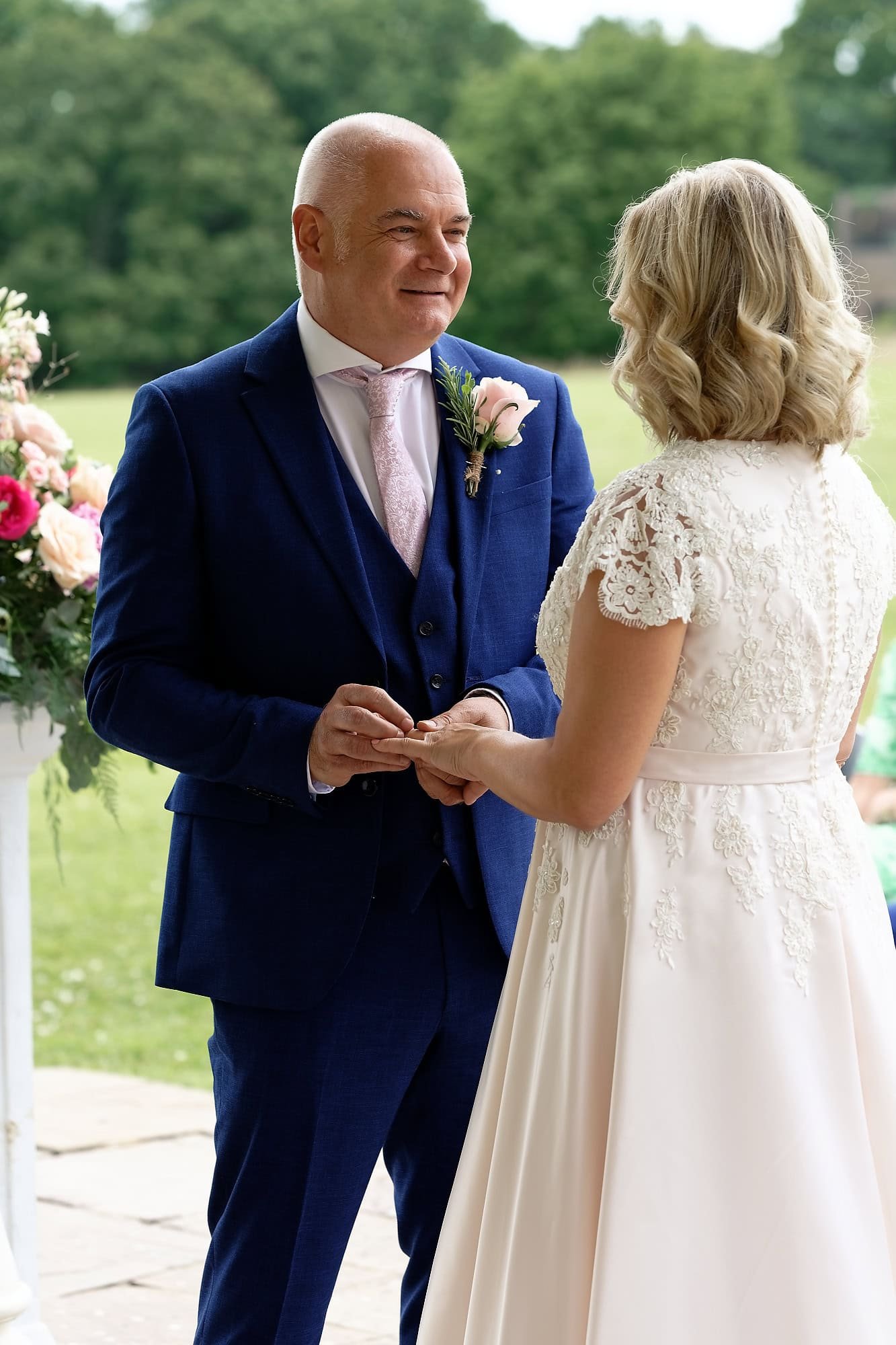 Groom placing the wedding ring on the bride's finger during their outdoor ceremony at South Lodge Hotel, Horsham