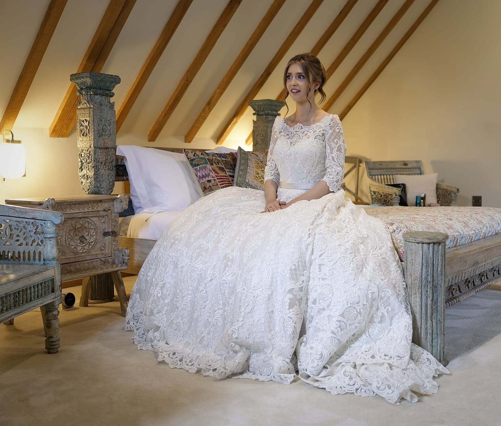 Bride sitting on bed waiting for bridesmaids to see her in dress for first time during bridal preparations at Trading Boundaries Sussex