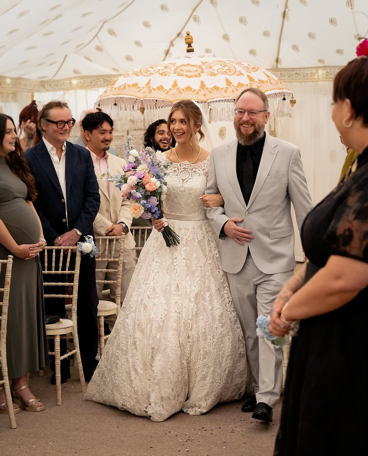 Bride walking down aisle, smiling at the guests, arm in arm with her father at Trading Boundaries wedding venue