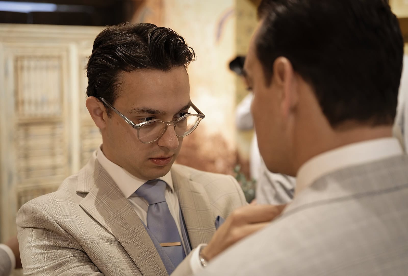 Groom pinning buttonhole on to groomsman's lapel at Trading Boundaries wedding venue