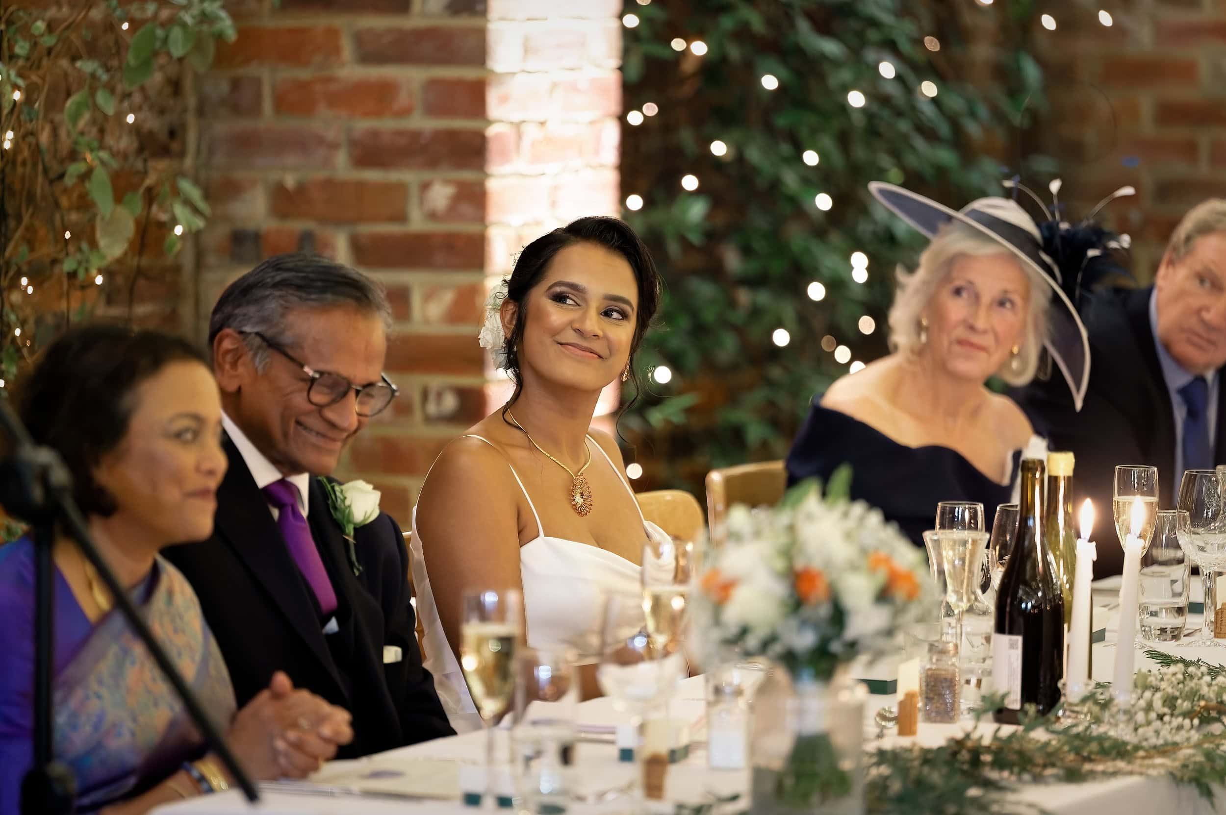 Candid portrait of bride smiling during wedding speeches at the top table in the Orangery at Northbrook Park wedding venue in Hampshire by Andy Kerr Photography