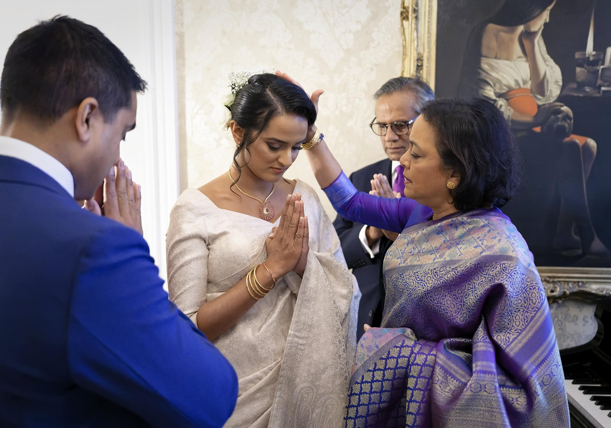 Bride receiving a private family blessing by the piano in the manor house at Northbrook Park wedding venue in Hampshire by Andy Kerr Photography