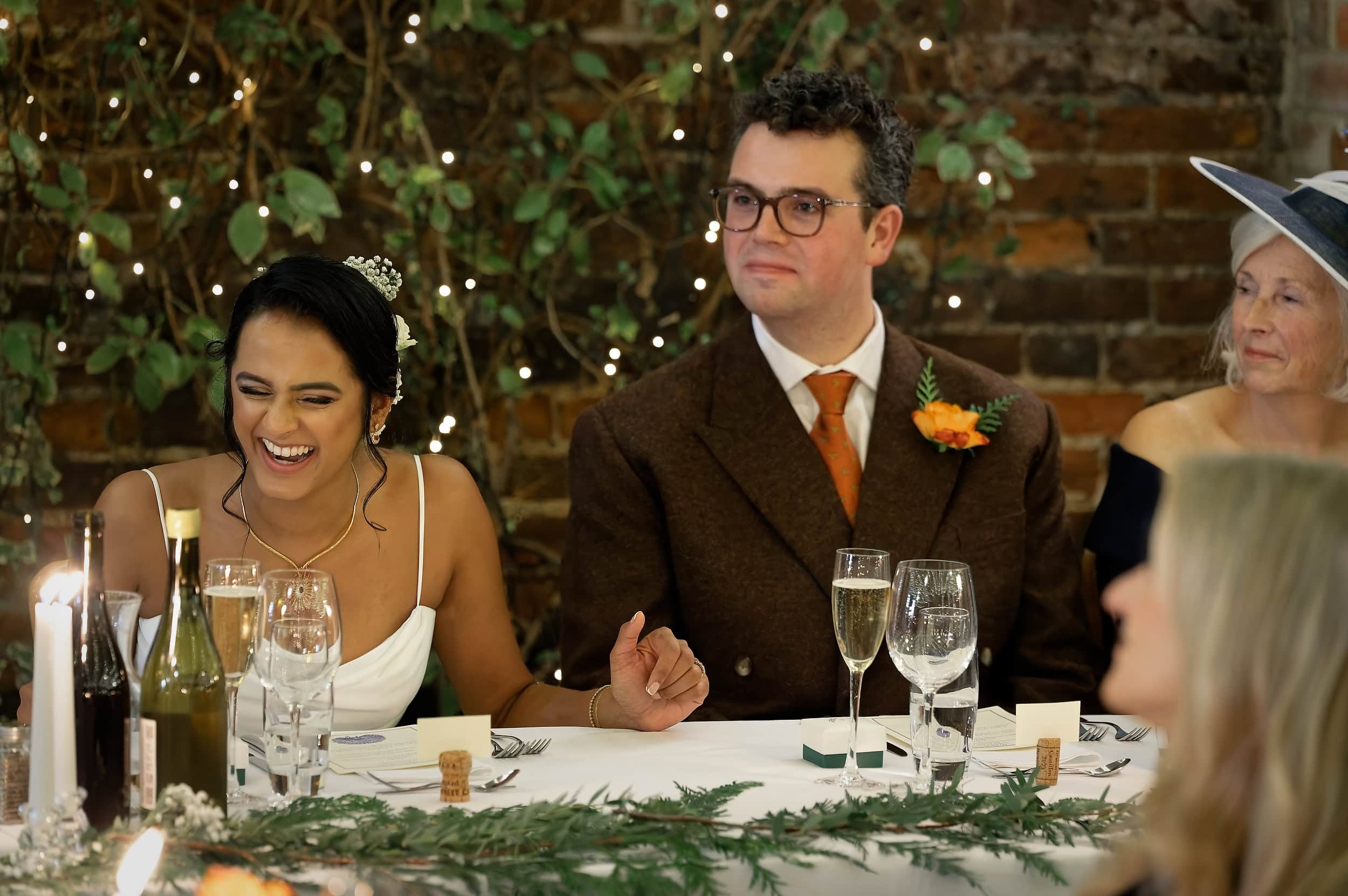 Bride laughing and groom reacting during wedding speeches in the Orangery at Northbrook Park wedding venue in Hampshire by Andy Kerr Photography