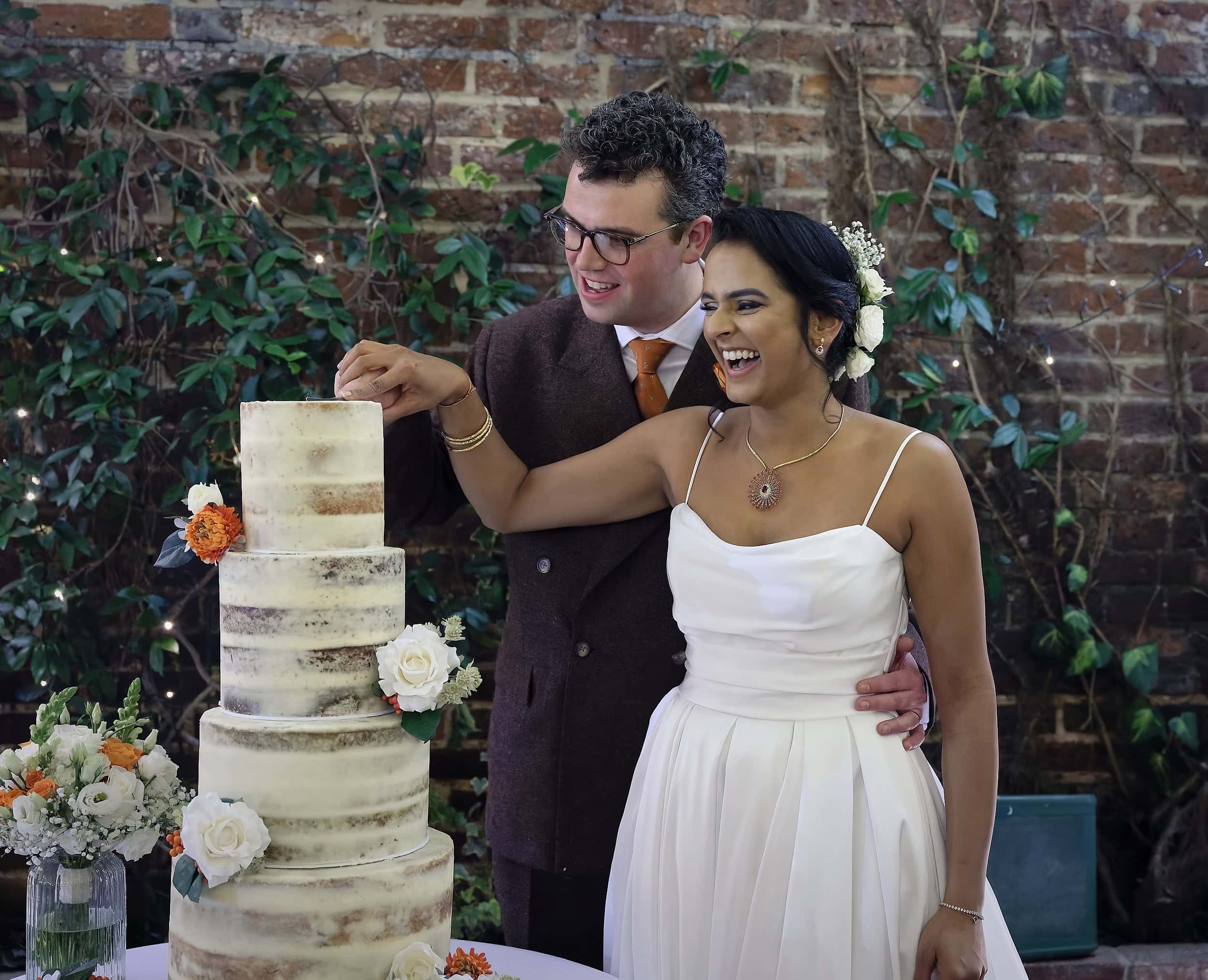 Bride and groom laughing during wedding cake cutting in the Orangery at Northbrook Park wedding venue in Hampshire by Andy Kerr Photography