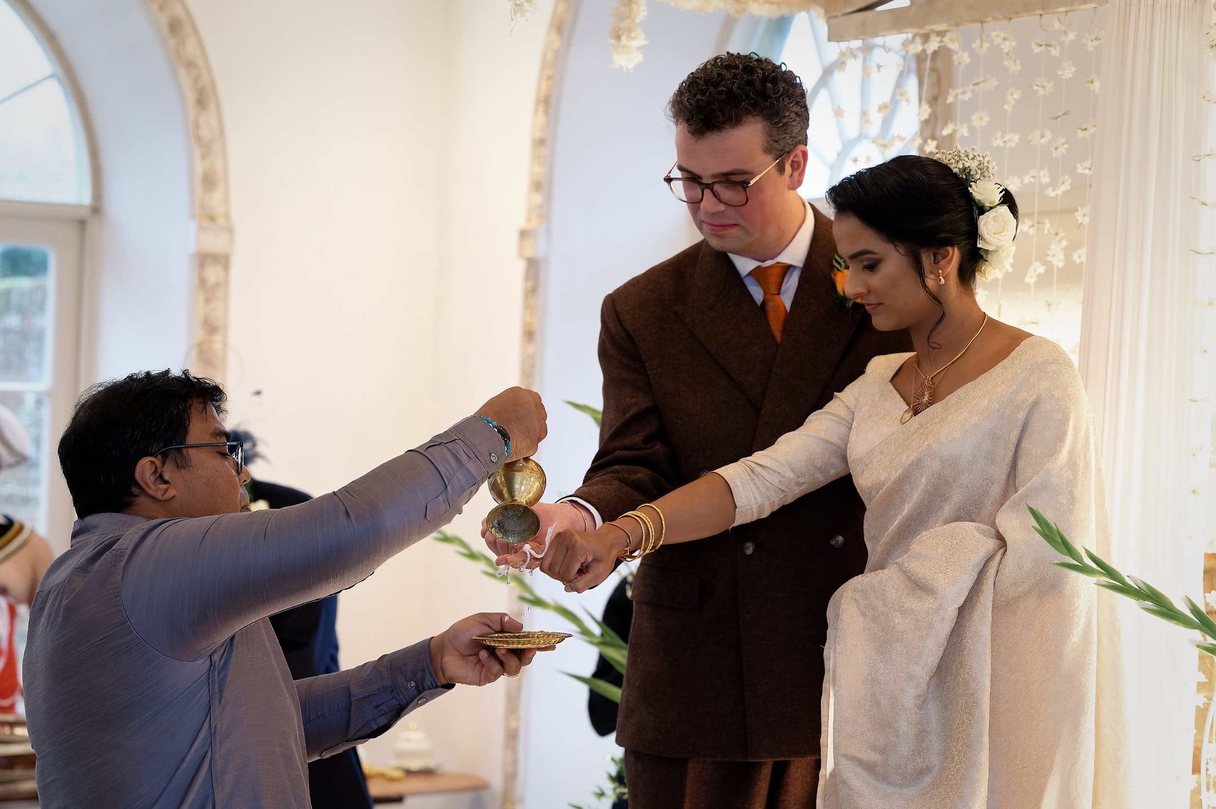 Bride and groom during the traditional water pouring ritual at the Poruwa in the Vine Room at Northbrook Park wedding venue in Hampshire by Andy Kerr Photography