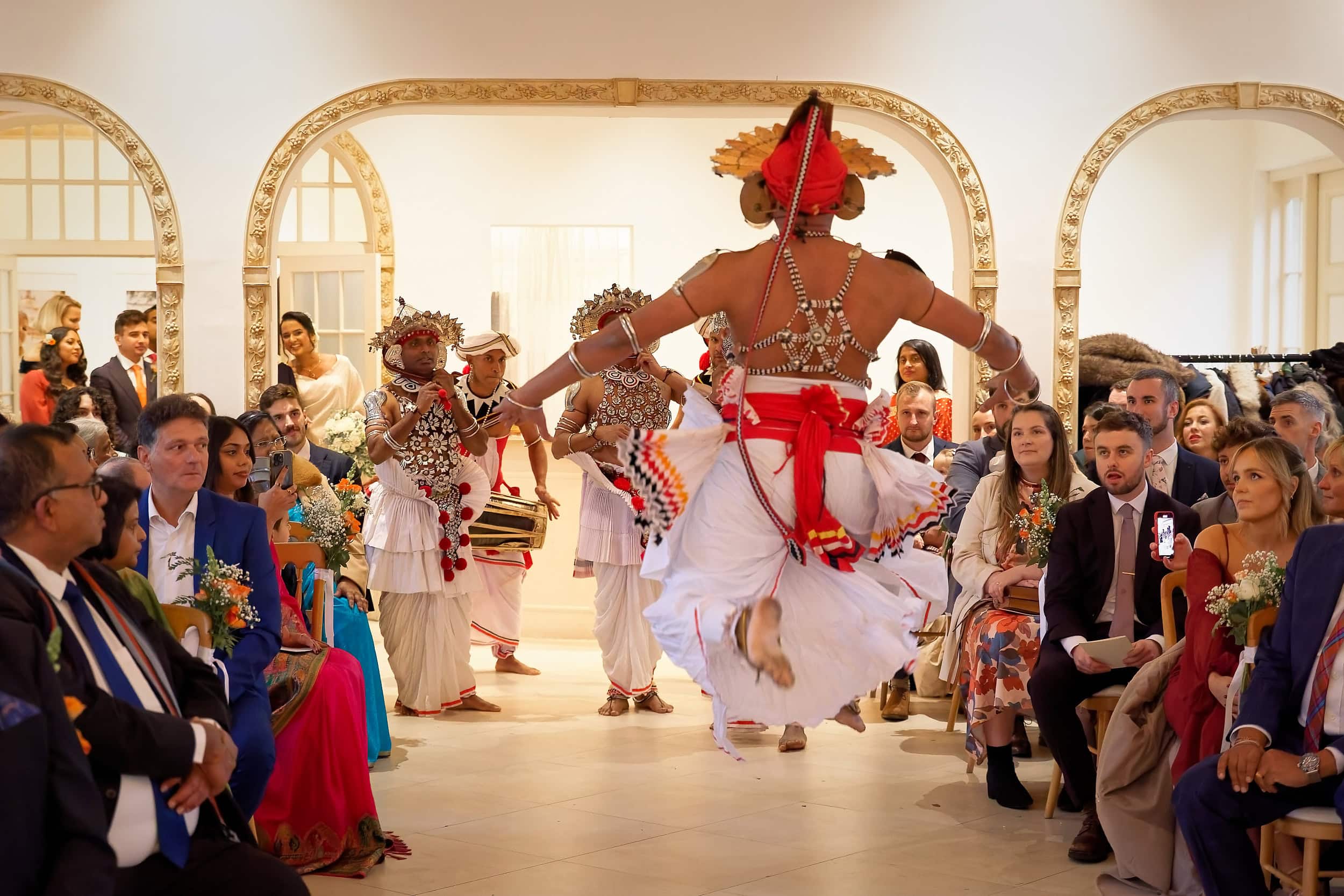 Traditional Sri Lankan dancer performing in the aisle during the wedding ceremony in the Vine Room at Northbrook Park wedding venue in Hampshire by Andy Kerr Photography