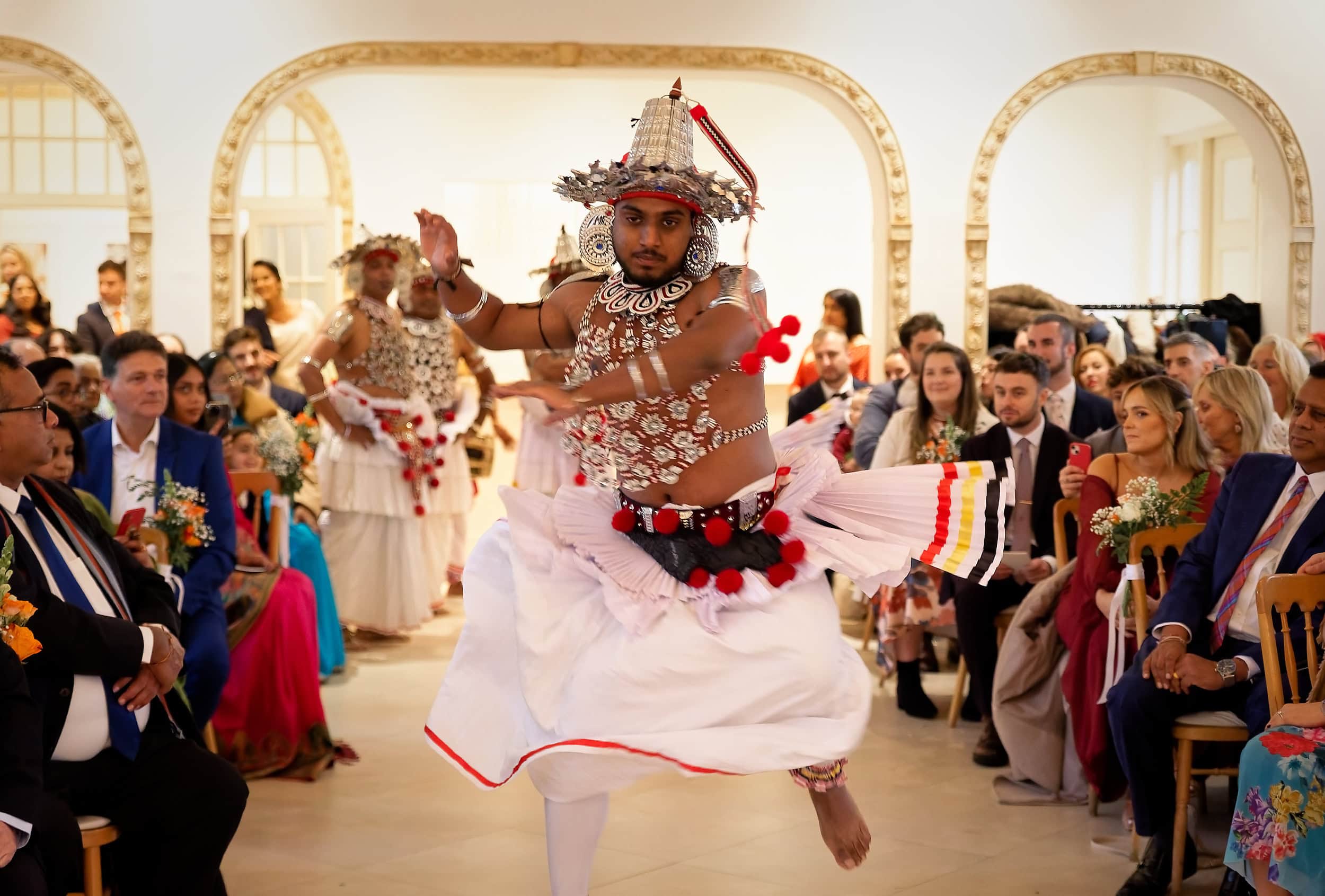 Traditional Sri Lankan dancer leaping during the wedding ceremony procession in the Vine Room at Northbrook Park wedding venue in Hampshire by Andy Kerr Photography