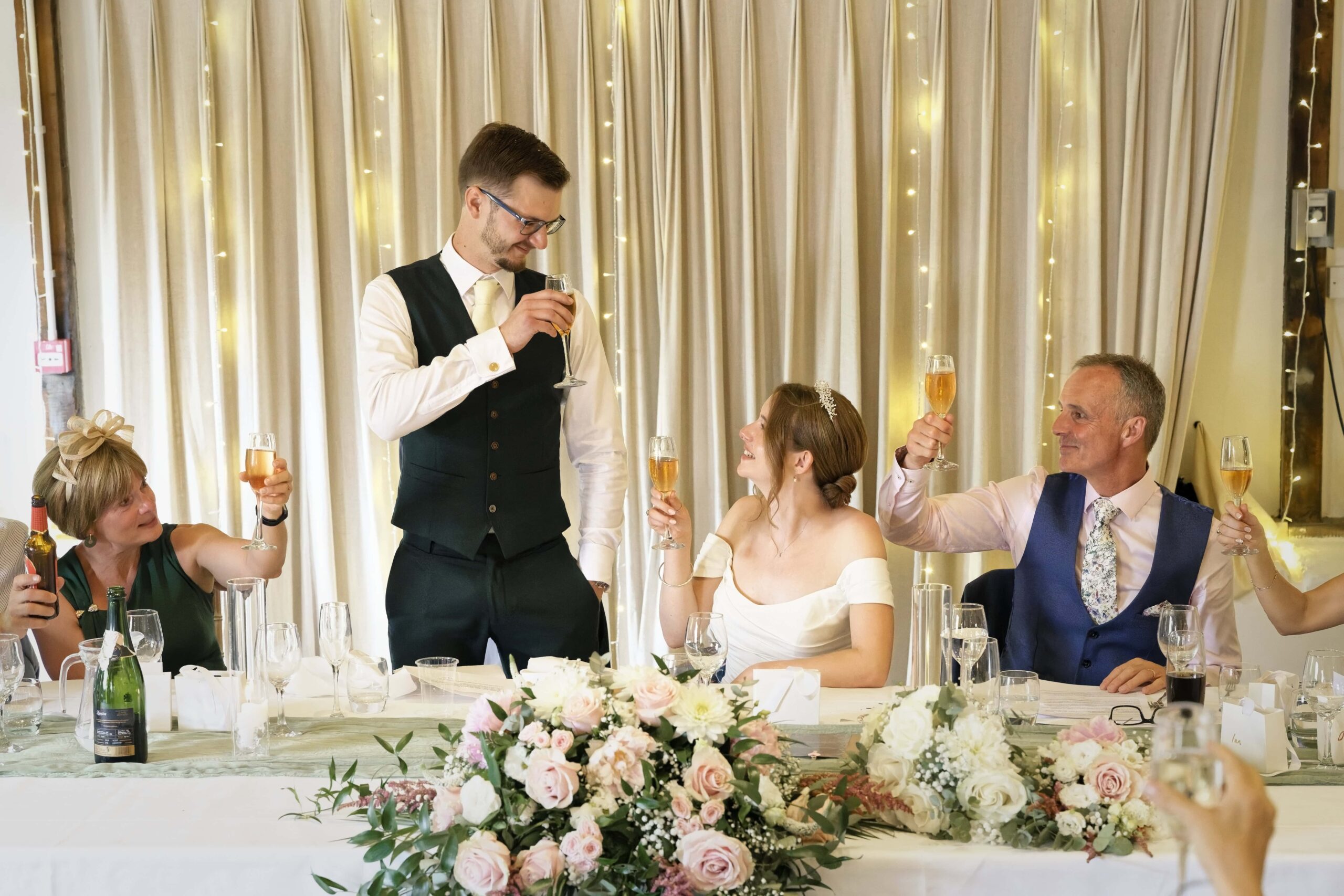 Fitzleroi Barn wedding photographer photo of the wedding party raising a champagne toast at the top table