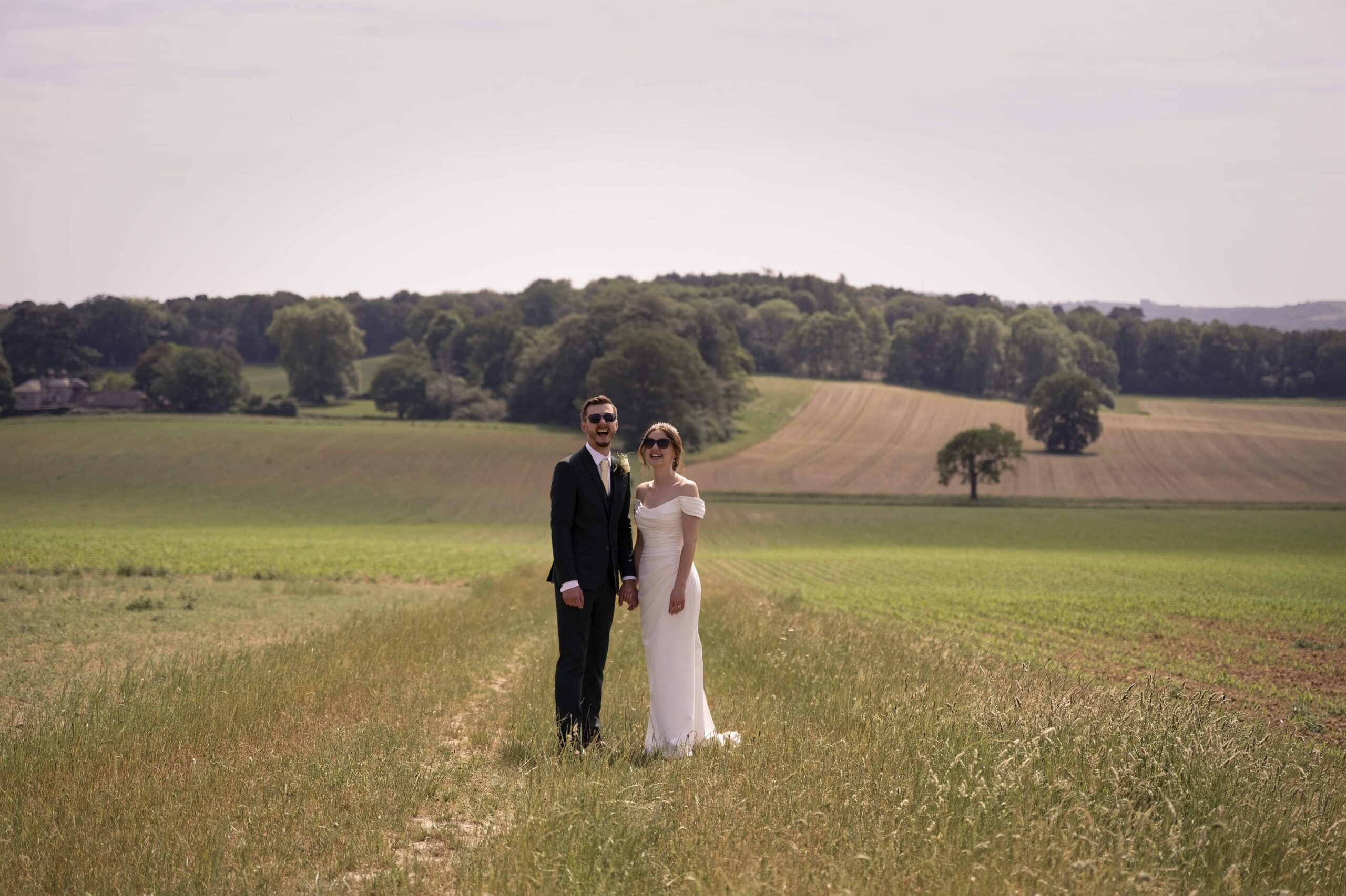 Fitzleroi Barn wedding photographer portrait of the newlyweds laughing together in a Sussex countryside field