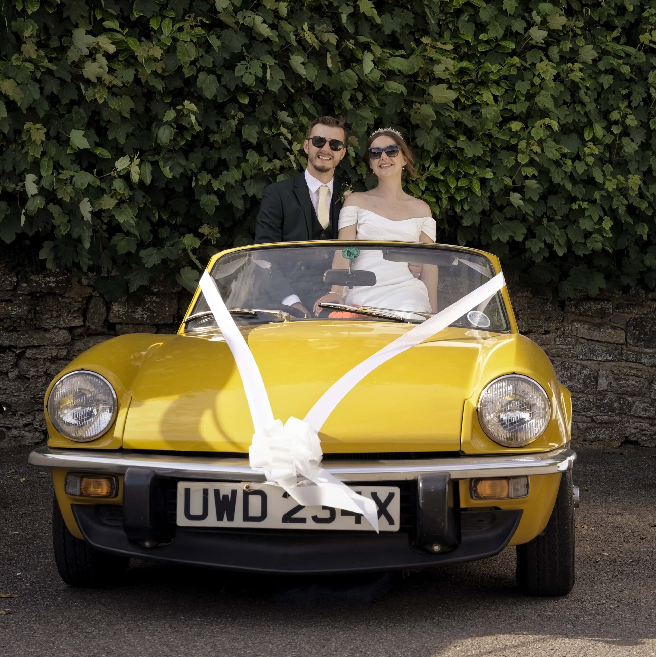 Fitzleroi Barn wedding photographer capturing the newlyweds in a vintage yellow convertible wedding car