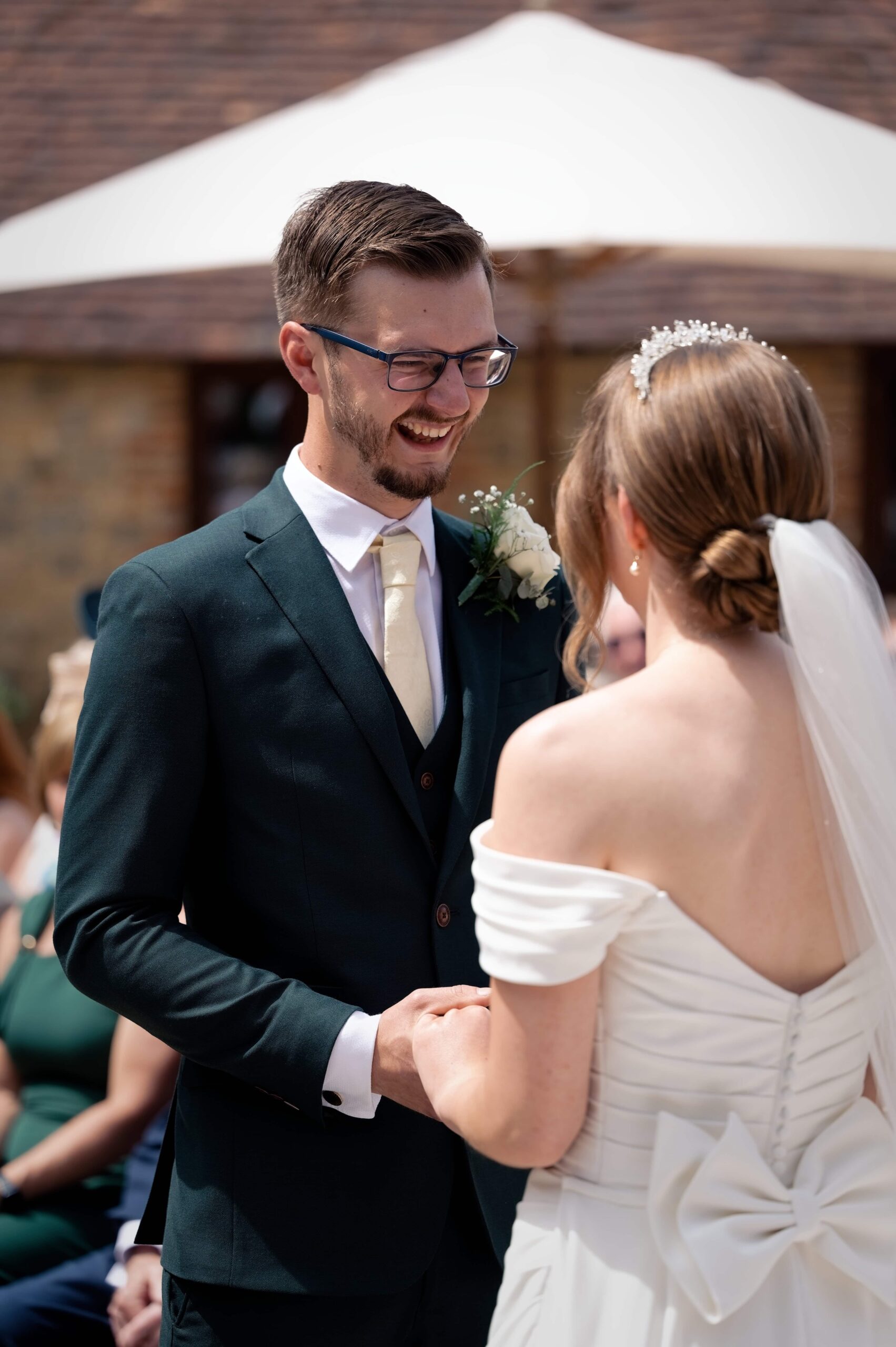 Fitzleroi Barn wedding photographer photo of the groom laughing while holding his bride's hand during the ceremony