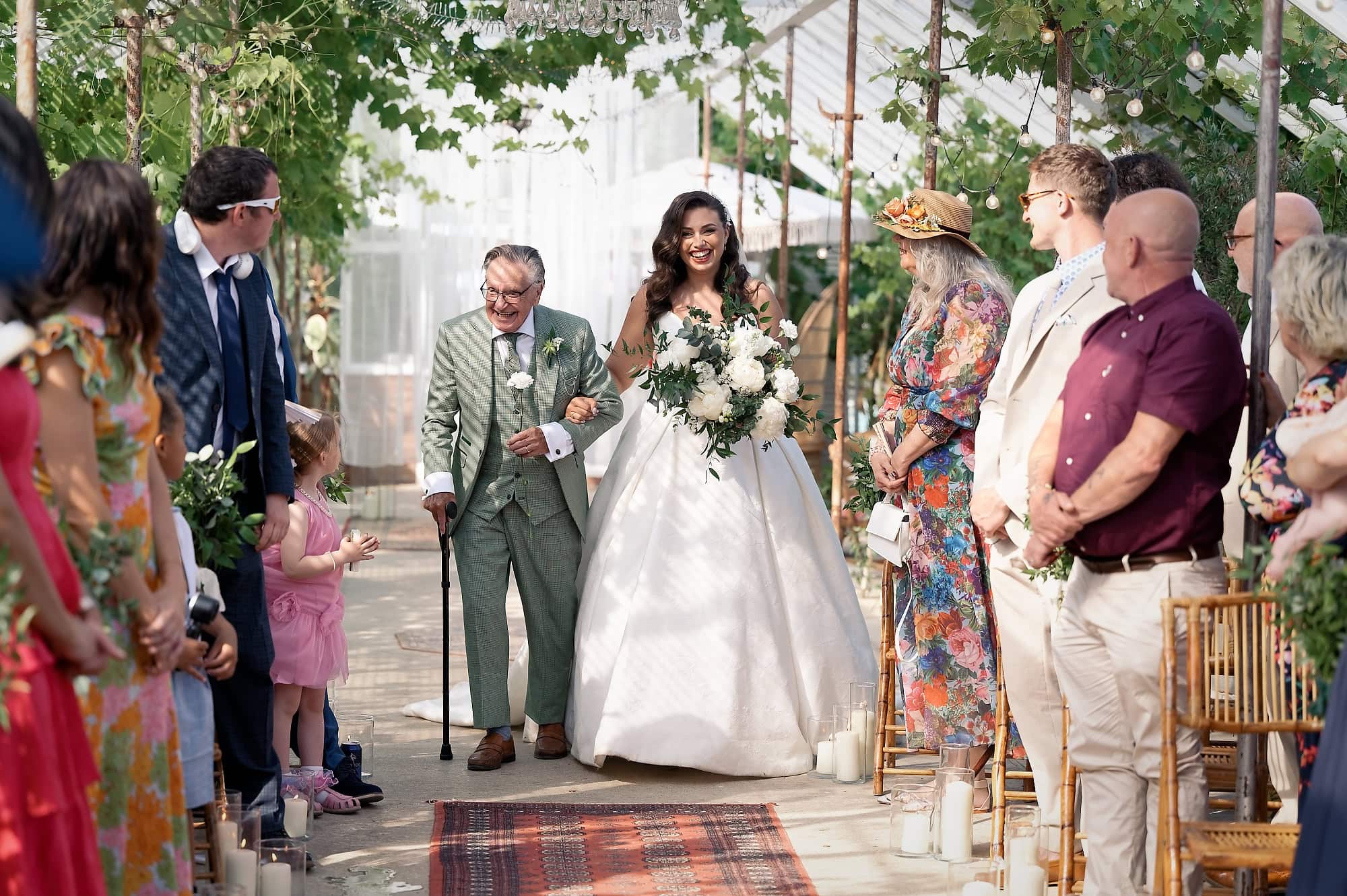 Bride walking down the aisle with her grandad as guests look on