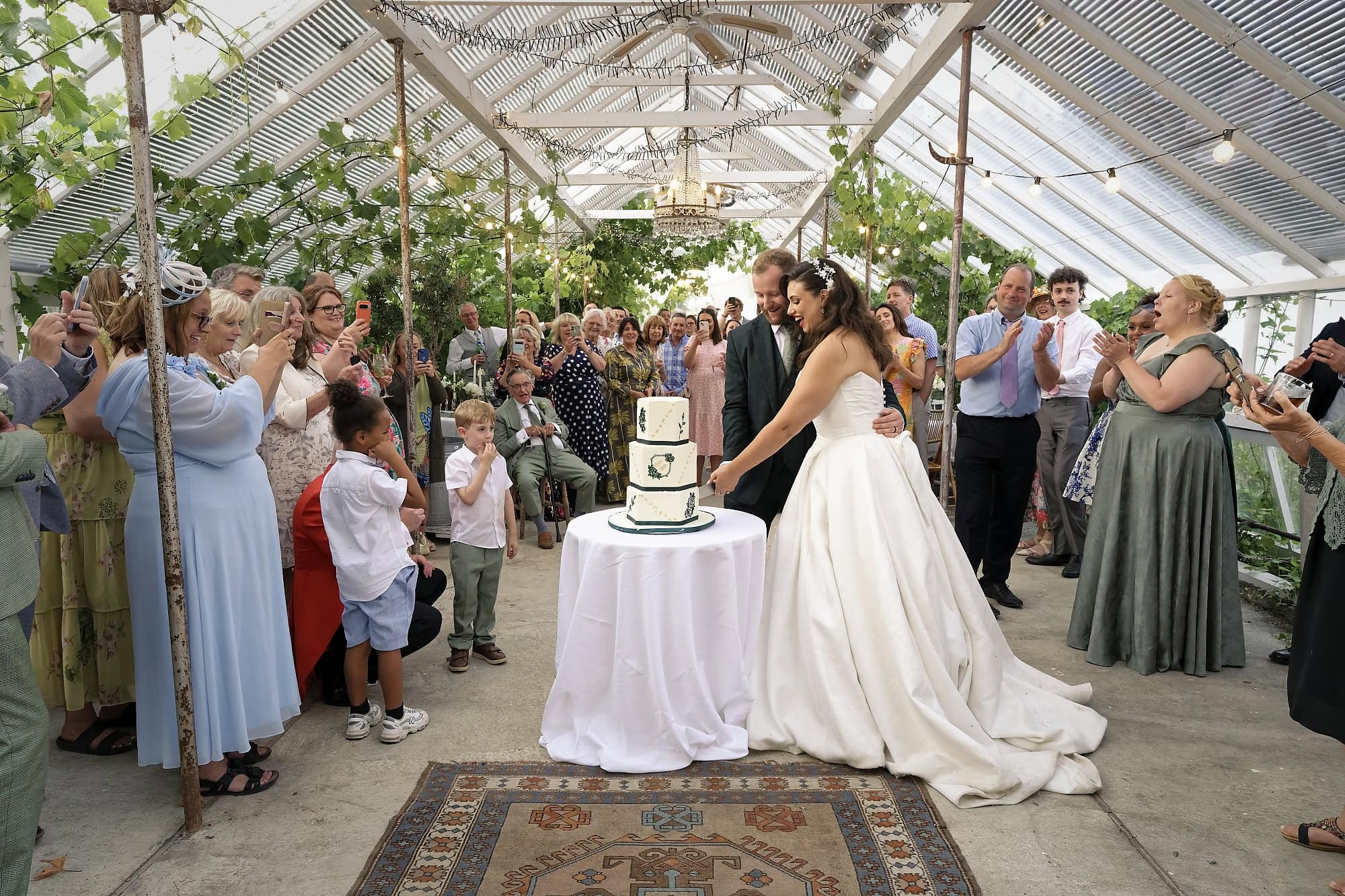 Wide view of guests applauding as the couple cut their wedding cake