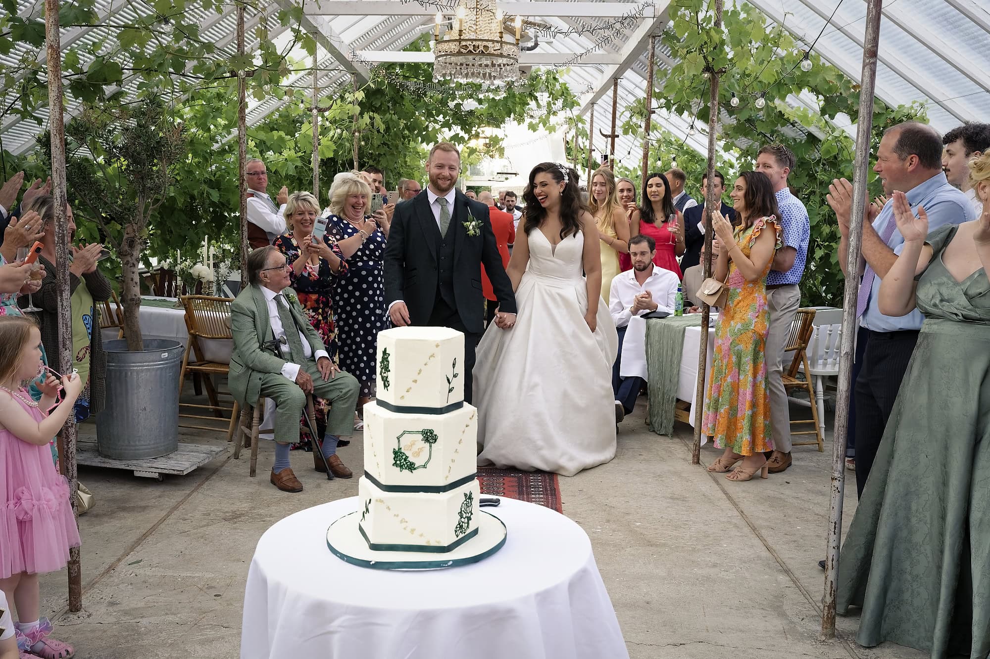 Bride and groom cutting their three-tier wedding cake inside the glasshouse