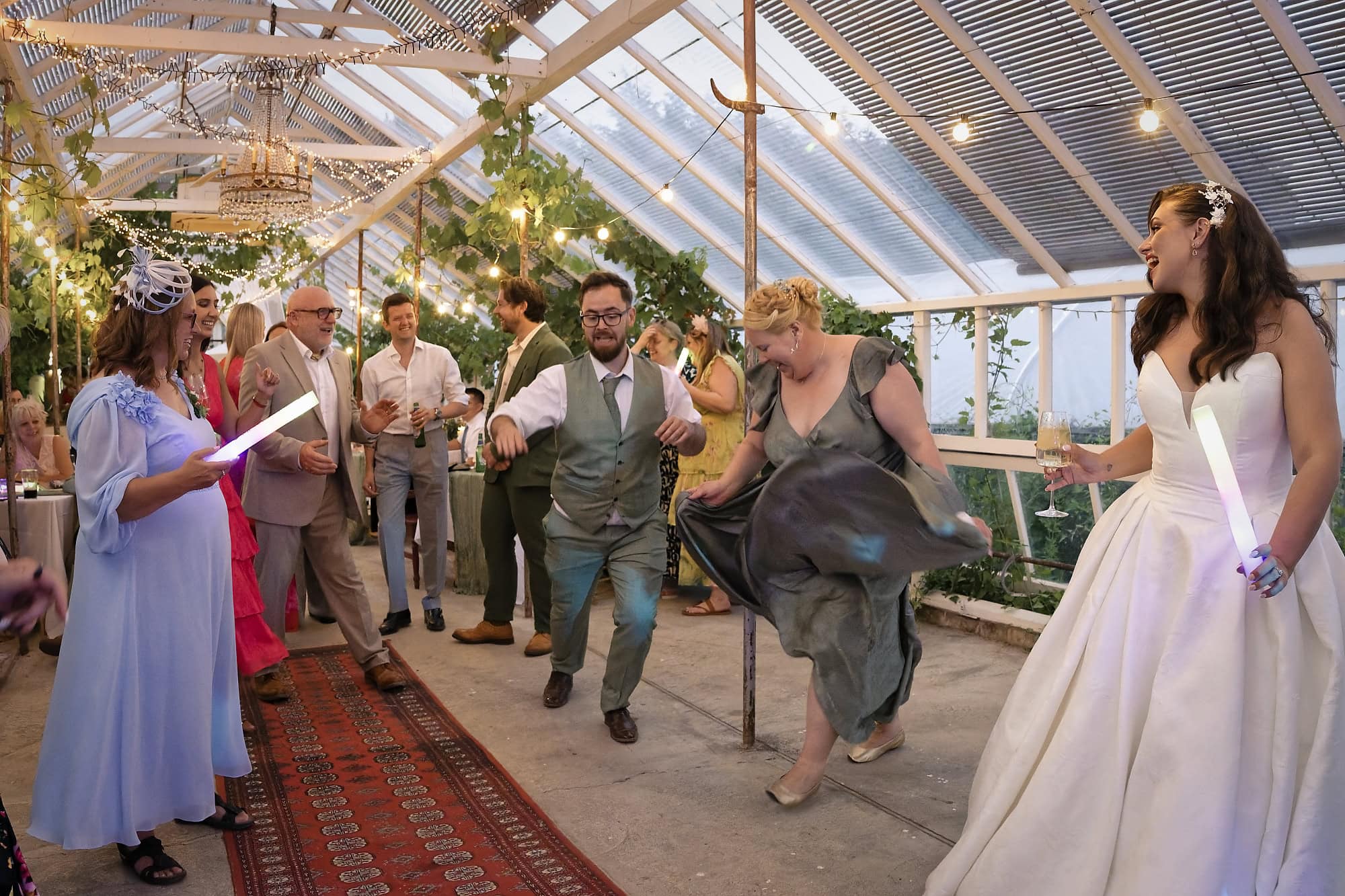 Wedding guests dancing with glow sticks under string lights in the evening