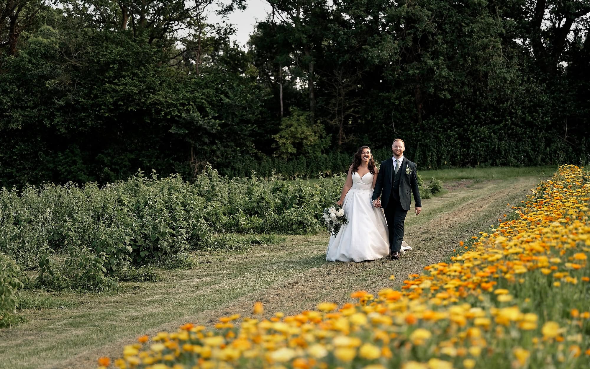 Bride and groom walking together next to sunflowers at Spring Gardens