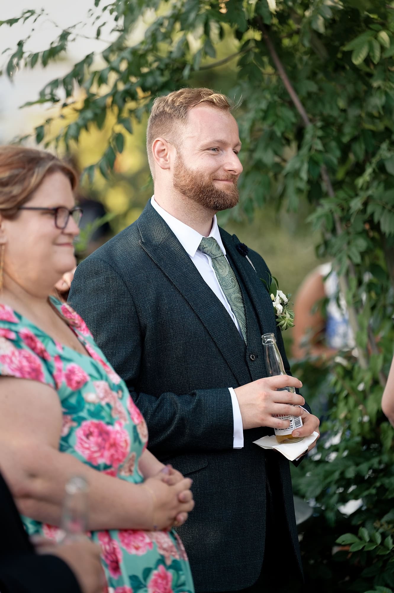 Groom smiling while listening to speeches with a drink in hand