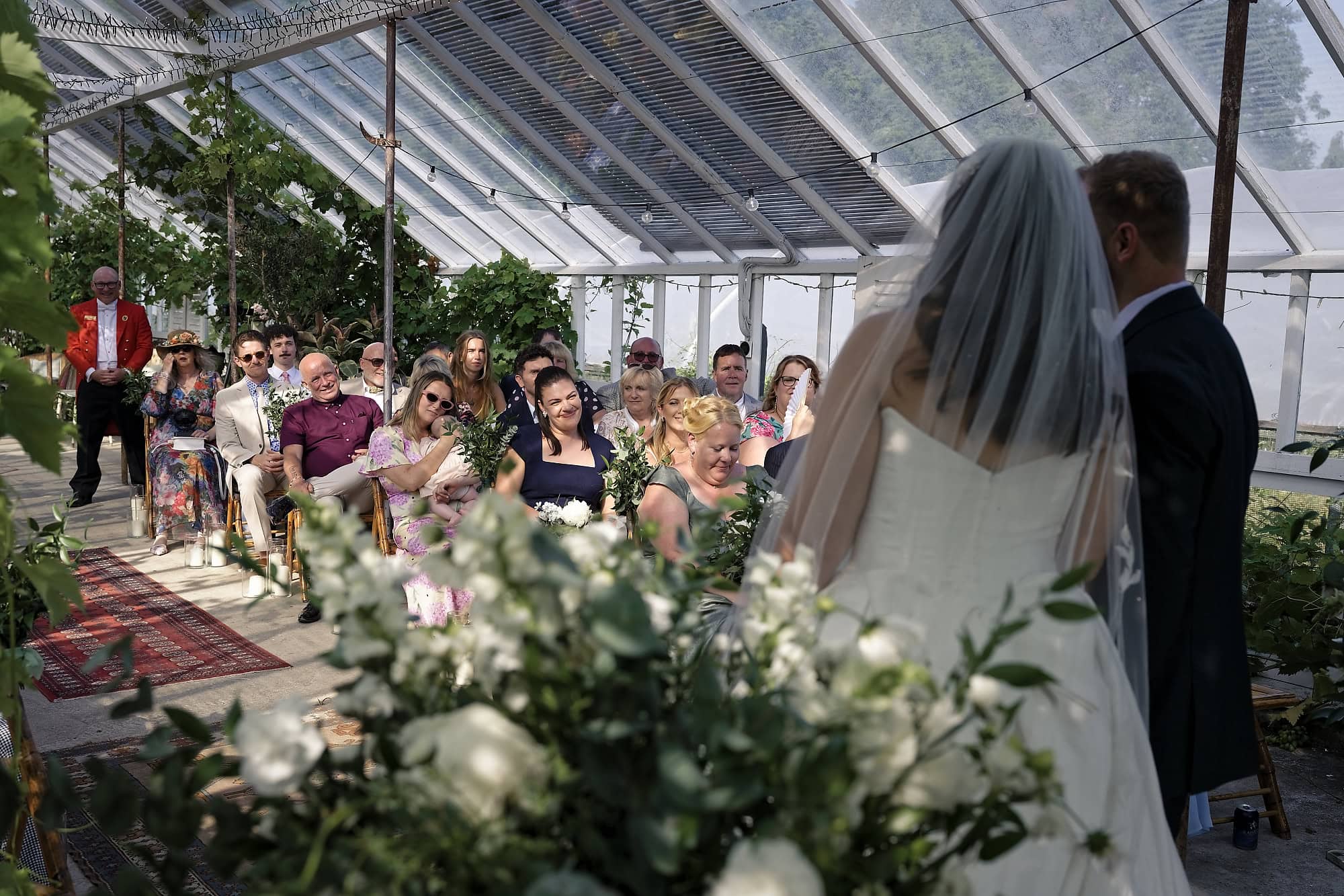 Guests smiling during the ceremony with the toastmaster visible at the back of the glasshouse