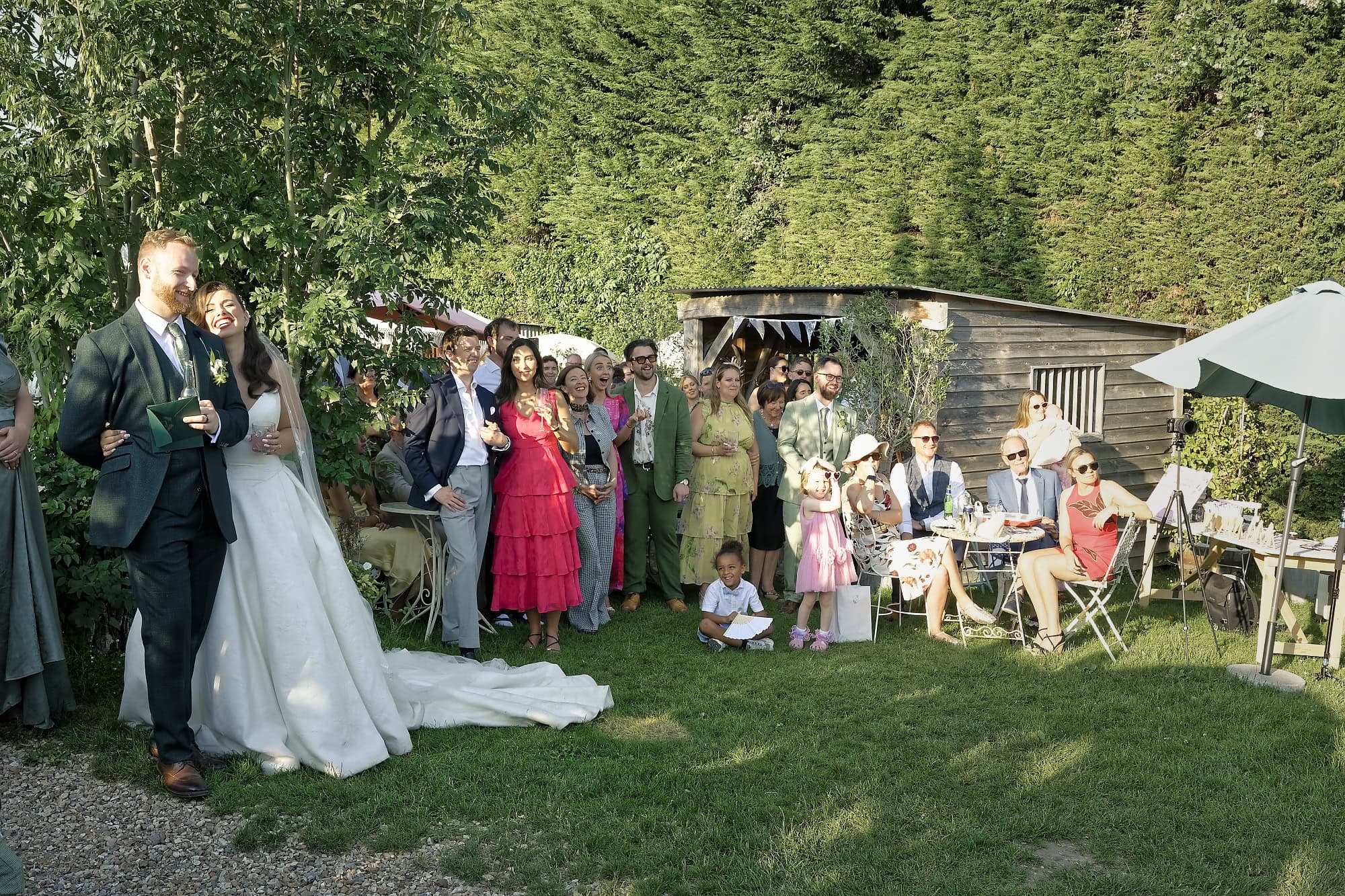 Newlyweds laughing with wedding guests gathered on the lawn
