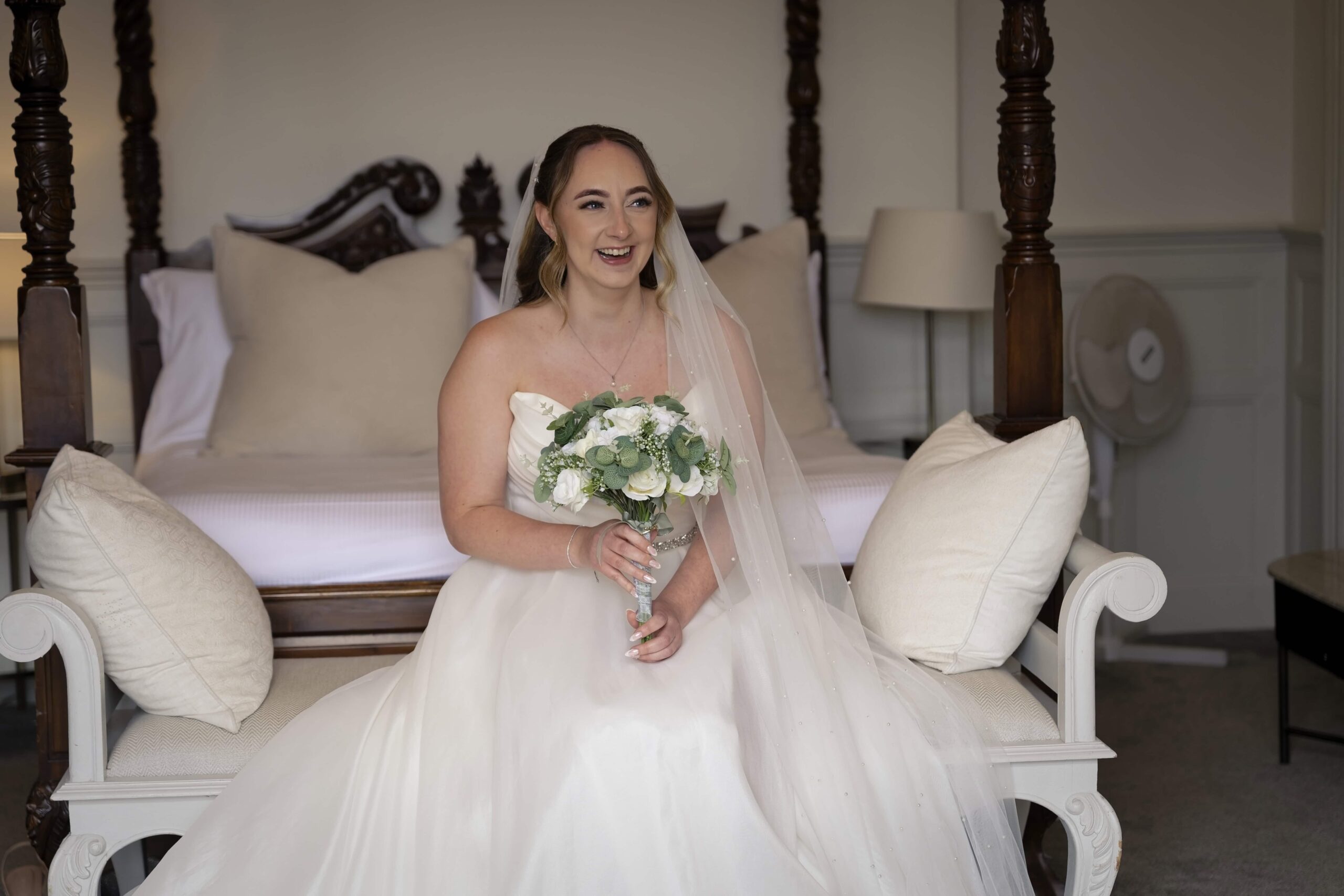 Bride smiling with her bouquet while seated in her getting-ready room at Highley Manor