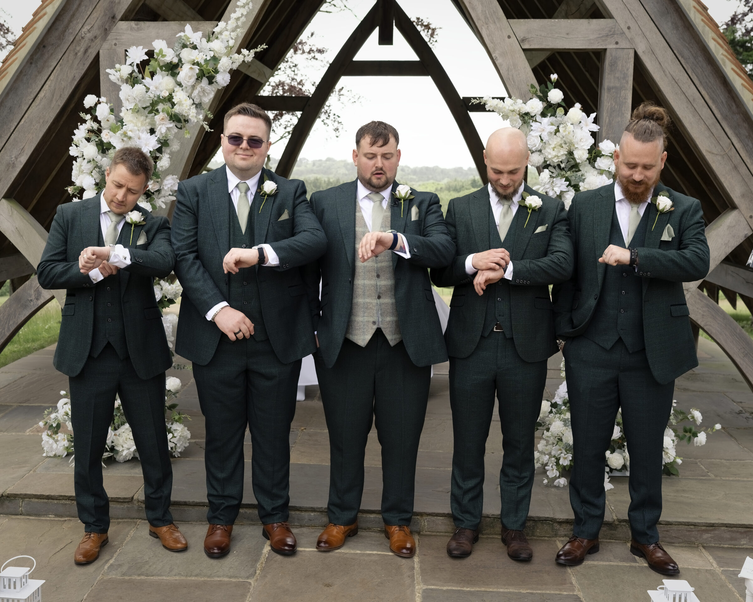Groom and groomsmen checking their watches under the timber pavilion at Highley Manor before the ceremony