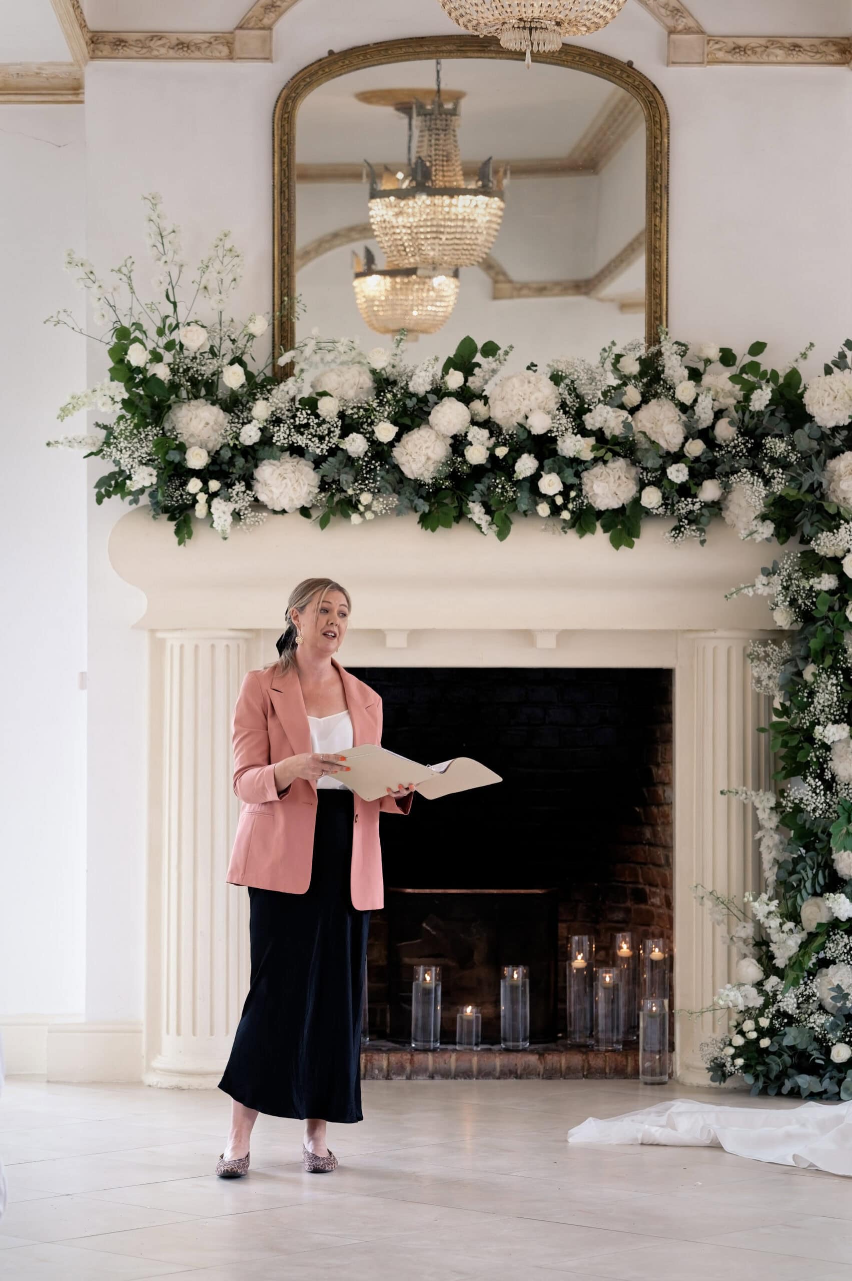 Celebrant leading the ceremony beside the flower-dressed fireplace