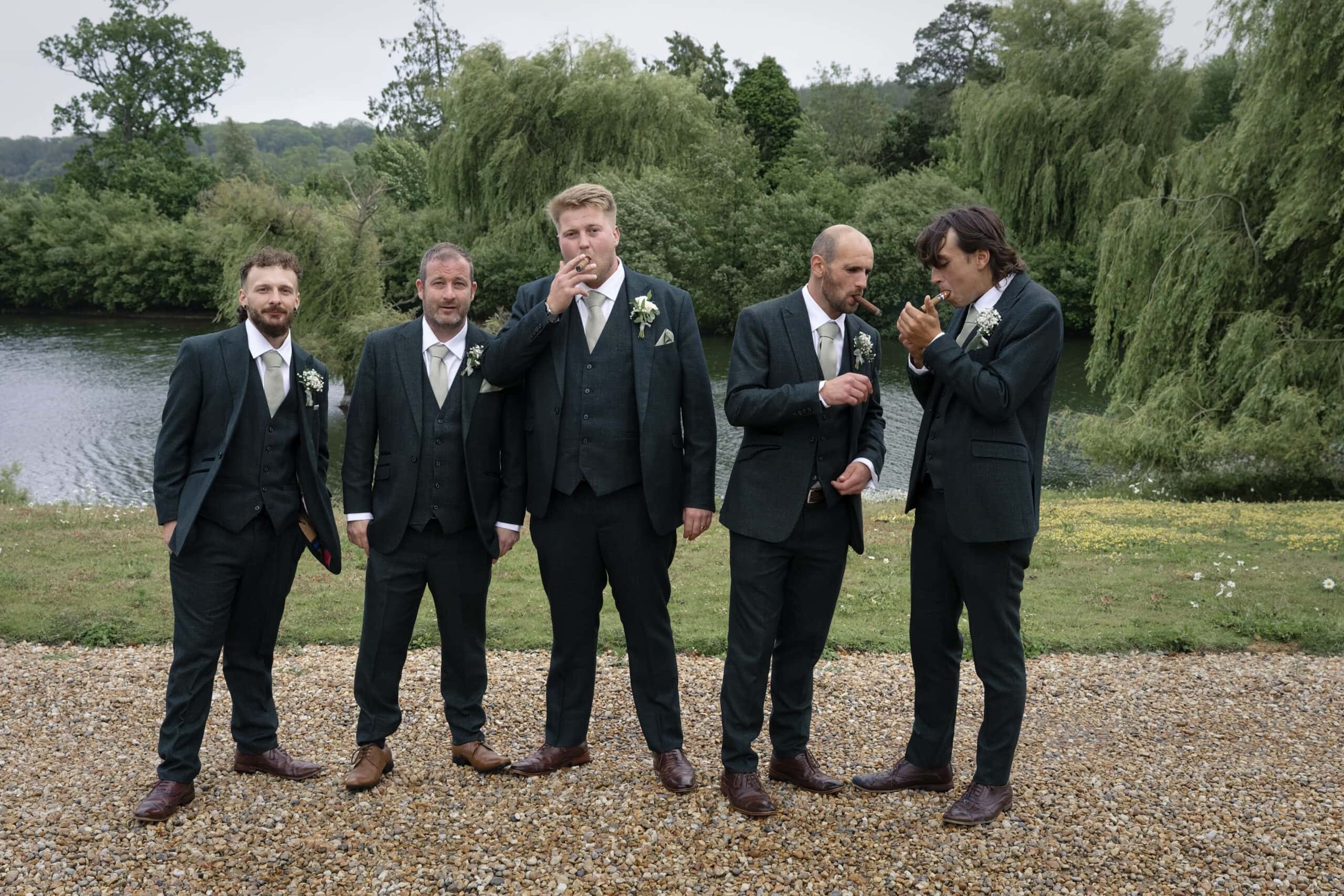 Groomsmen sharing cigars by the lake in the evening