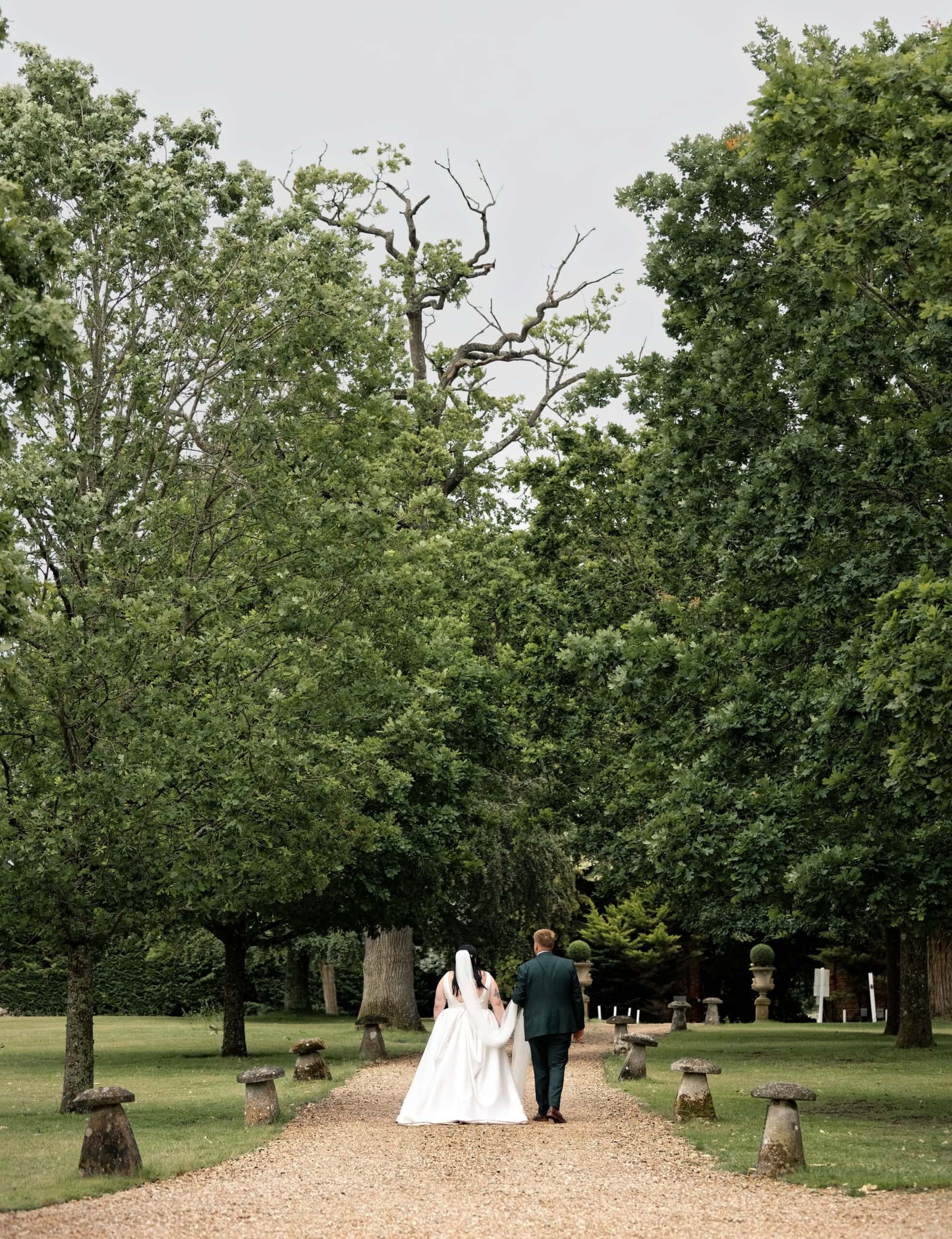 Bride and groom walking hand in hand along a tree-lined path