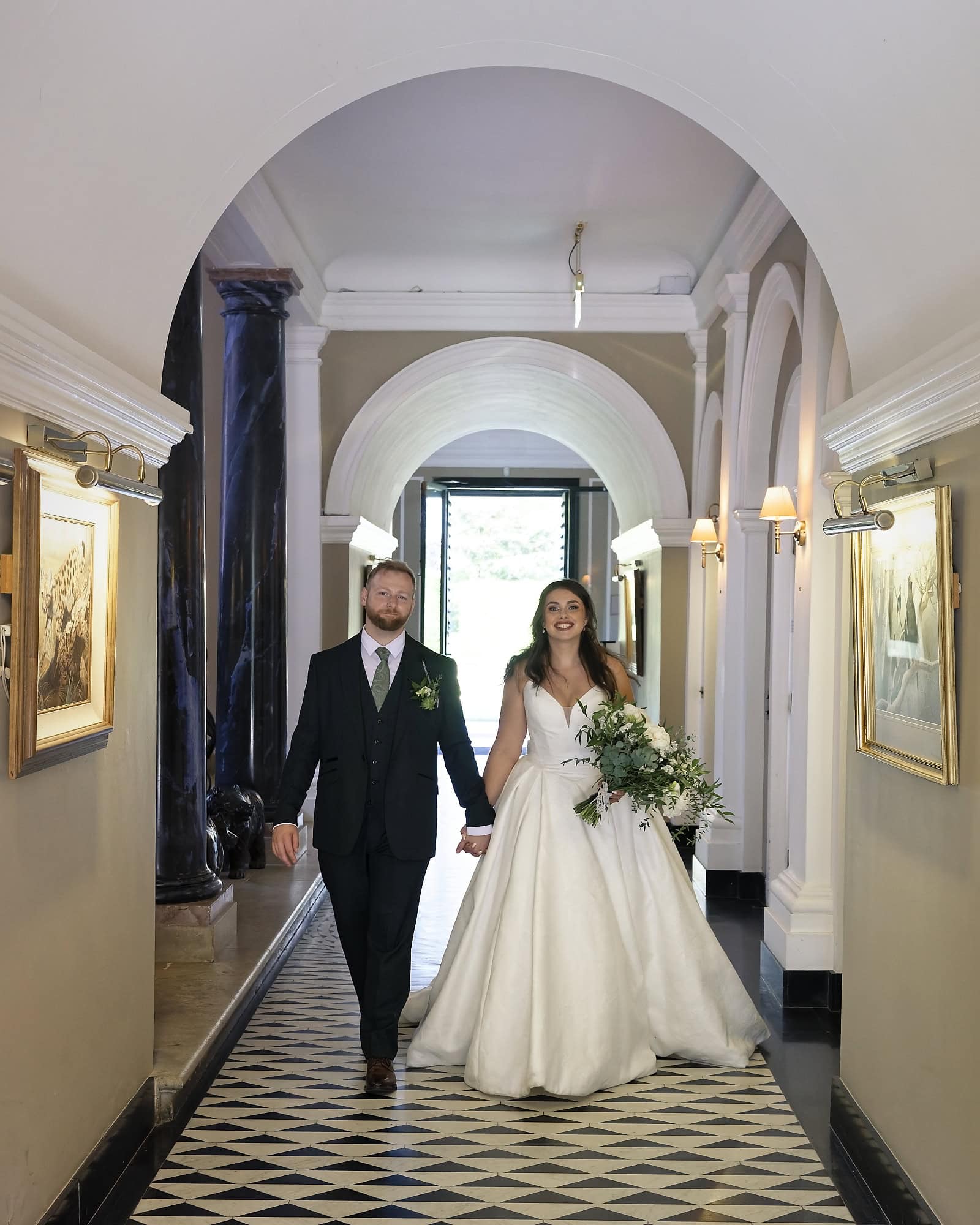 Bride and groom walking through the Port Lympne hotel's arched corridor
