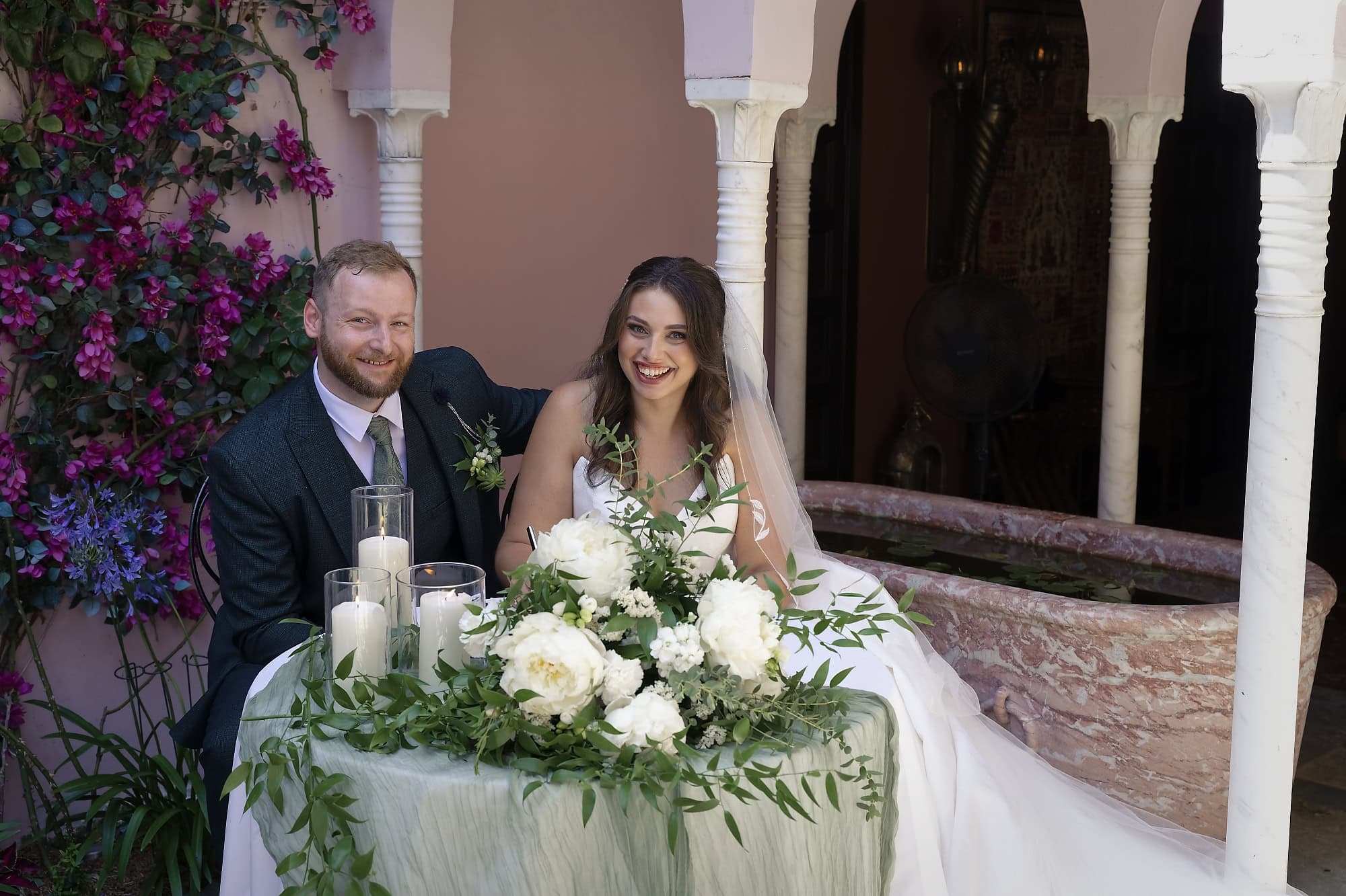 Bride and groom seated together at the flower-decked table in the Moroccan Courtyard after signing the marriage register