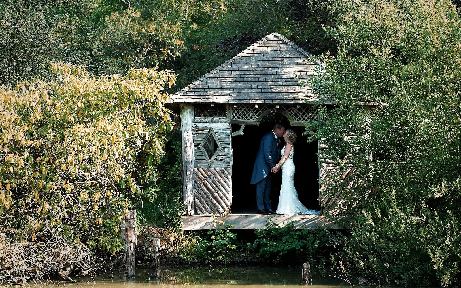 Bride and groom kissing inside the boathouse over the lake at The Ravenswood