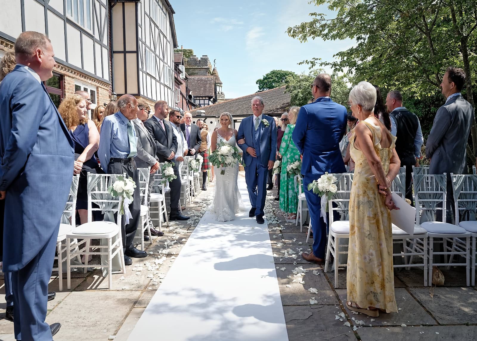 Bride walking down the aisle with her father in the sunshine at The Ravenswood