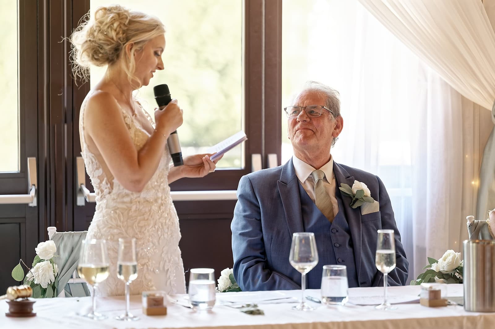 Bride speaking into a microphone as her father looks on at The Ravenswood