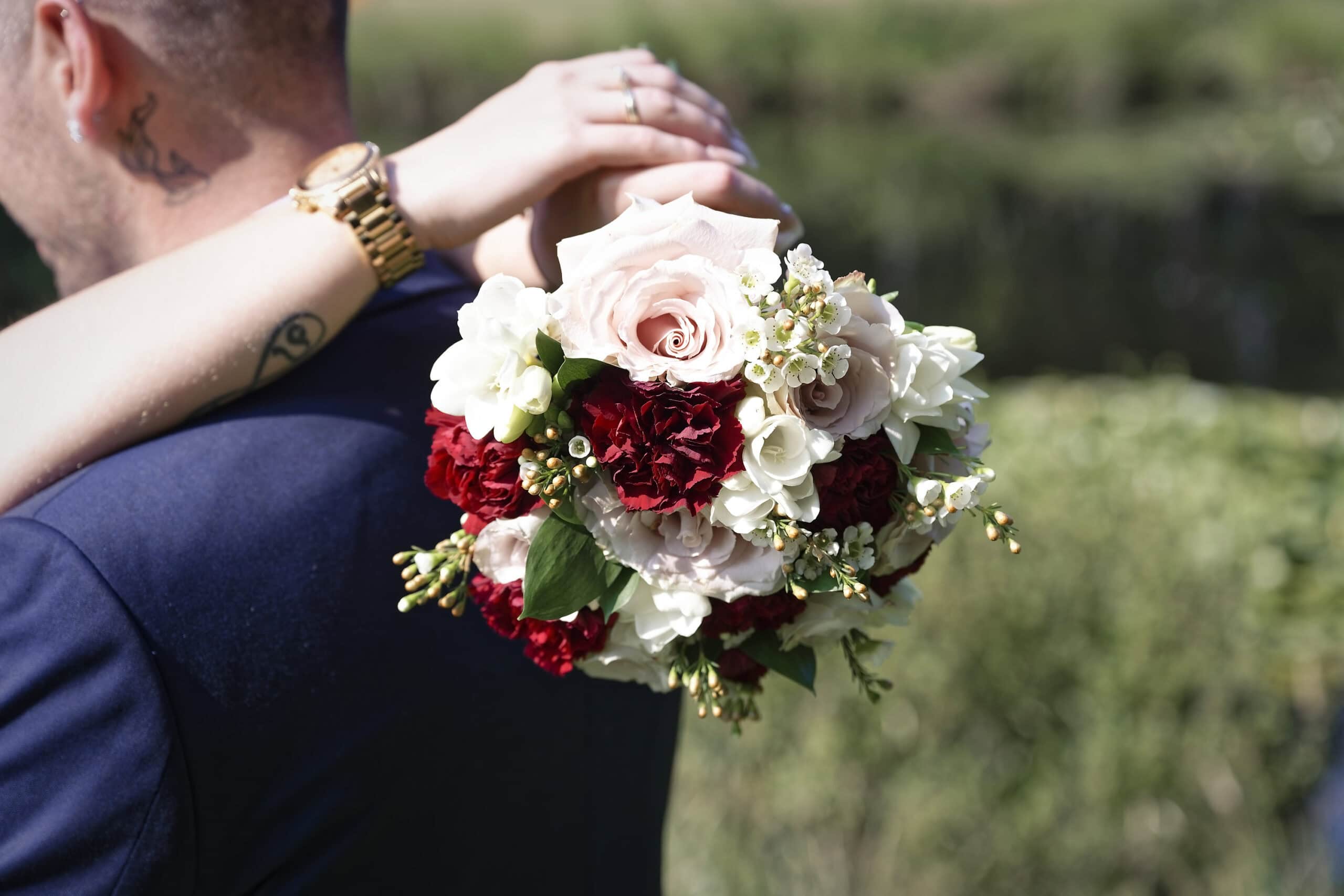 Close-up of the blush pink, red and white bridal bouquet held over the groom's shoulder at the Cottesmore Hotel