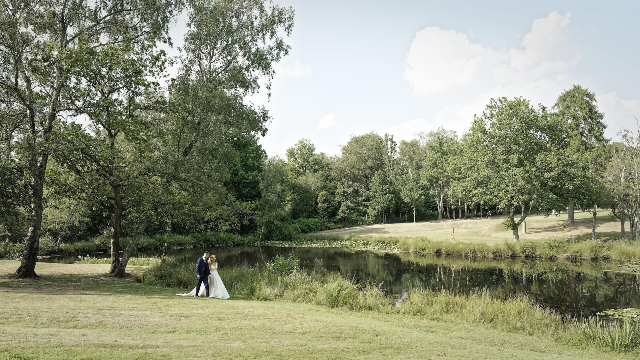 Bride and groom walking beside the lake on the golf course at the Cottesmore Hotel in West Sussex