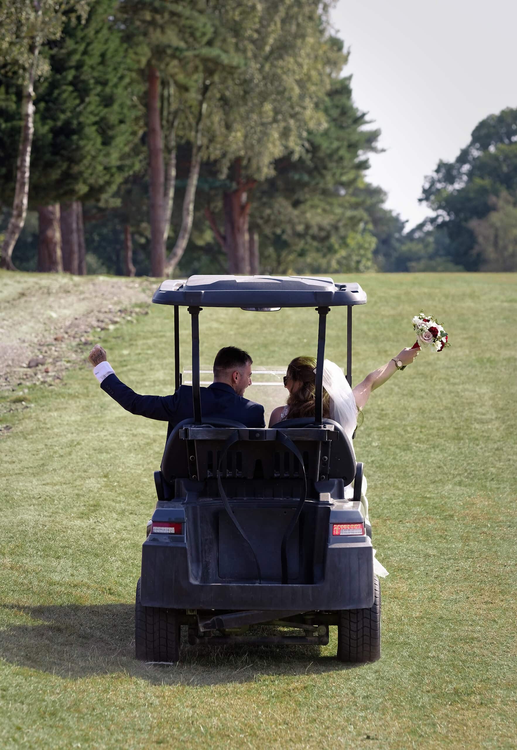 Bride and groom raising their arms and bouquet as they ride away in a golf buggy at the Cottesmore Hotel