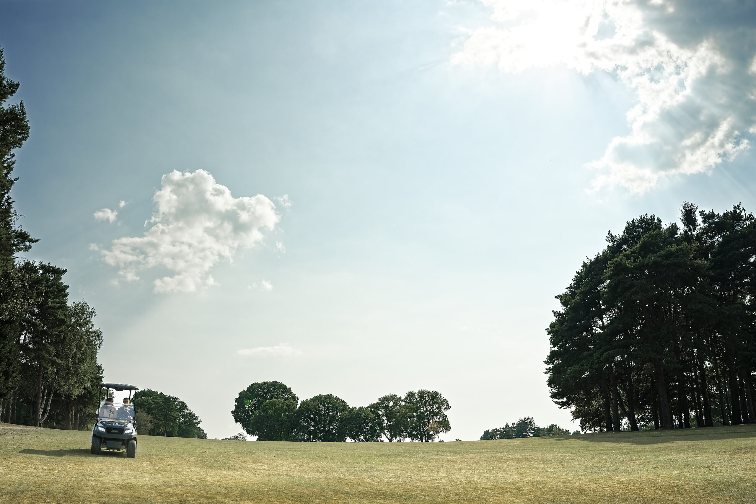 Golf buggy crossing the wide fairway under a big summer sky at the Cottesmore Hotel golf course