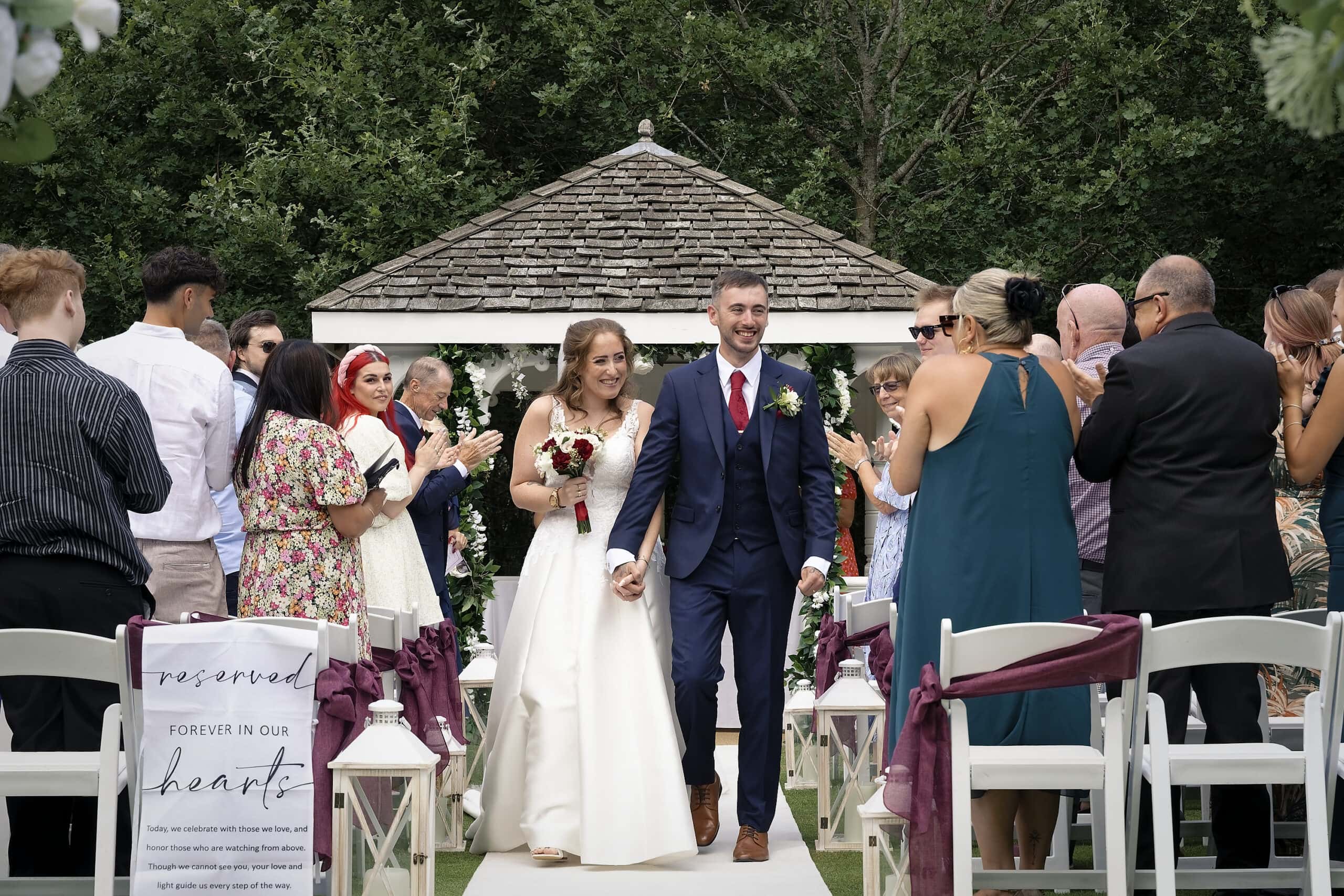 Bride and groom walking hand in hand back up the aisle past the gazebo as guests clap, by a Cottesmore Hotel wedding photographer