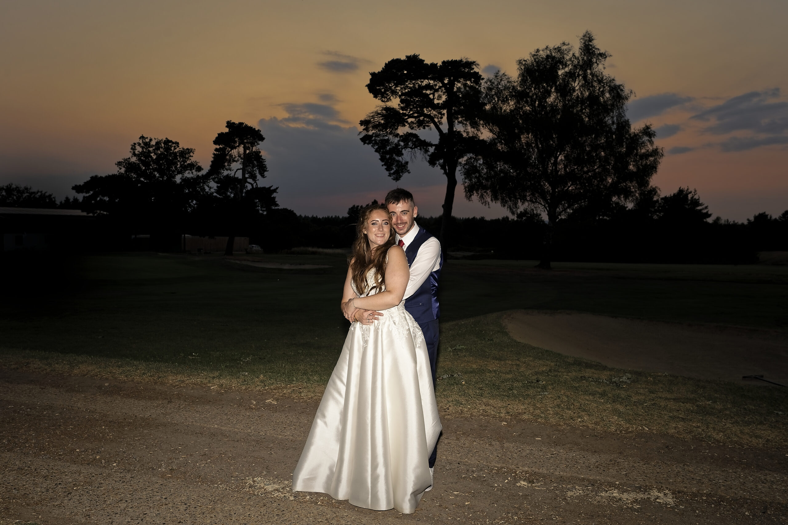 Bride and groom hugging against a golden sunset sky and silhouetted trees on the Cottesmore Hotel golf course