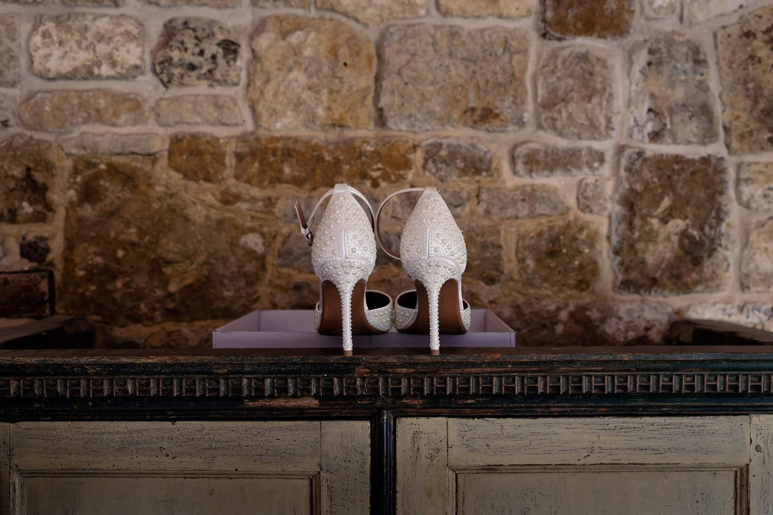 Sparkly bridal heels against an old stone wall, photographed by a Grittenham Barn wedding photographer