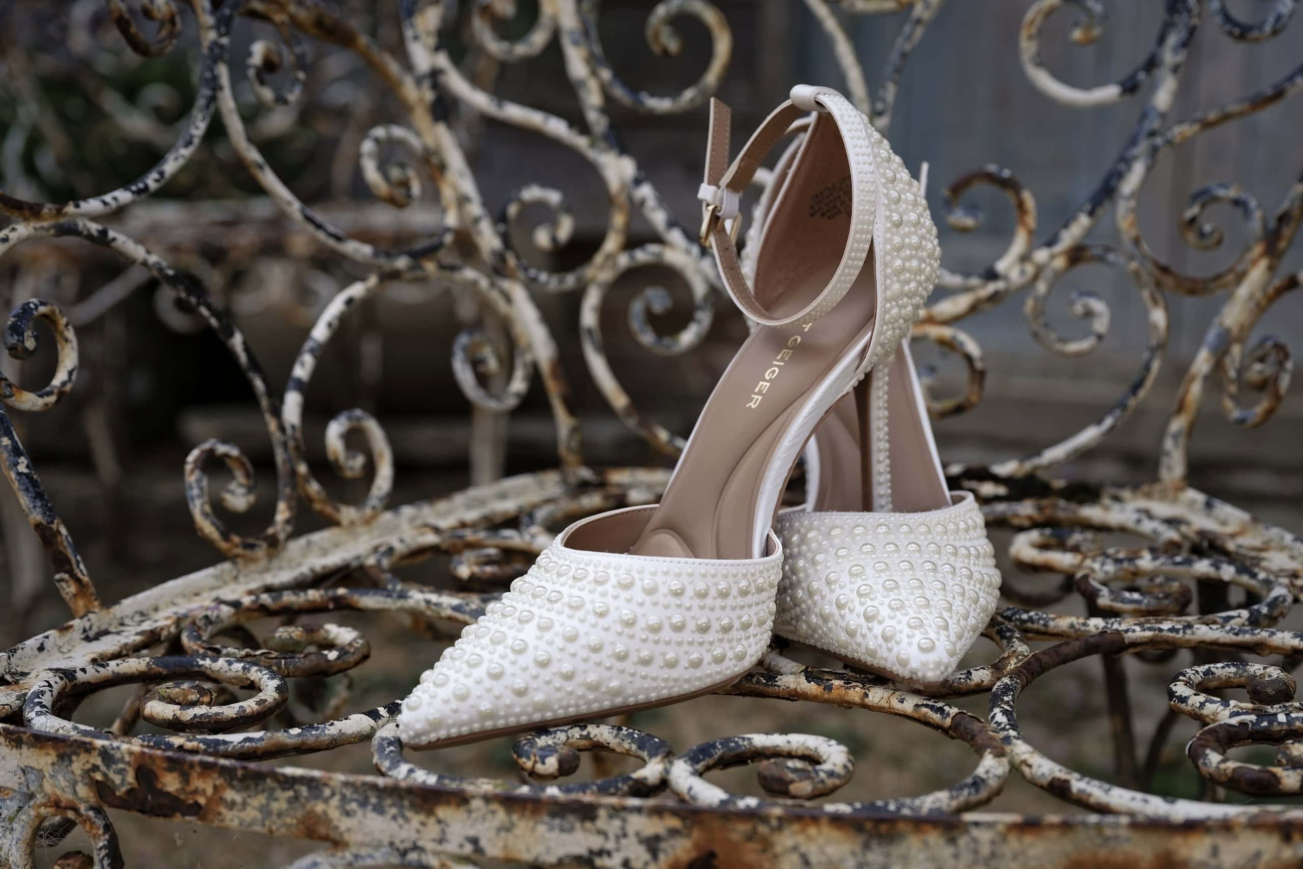 Pearl embellished bridal shoes resting on an ornate iron chair at Grittenham Barn