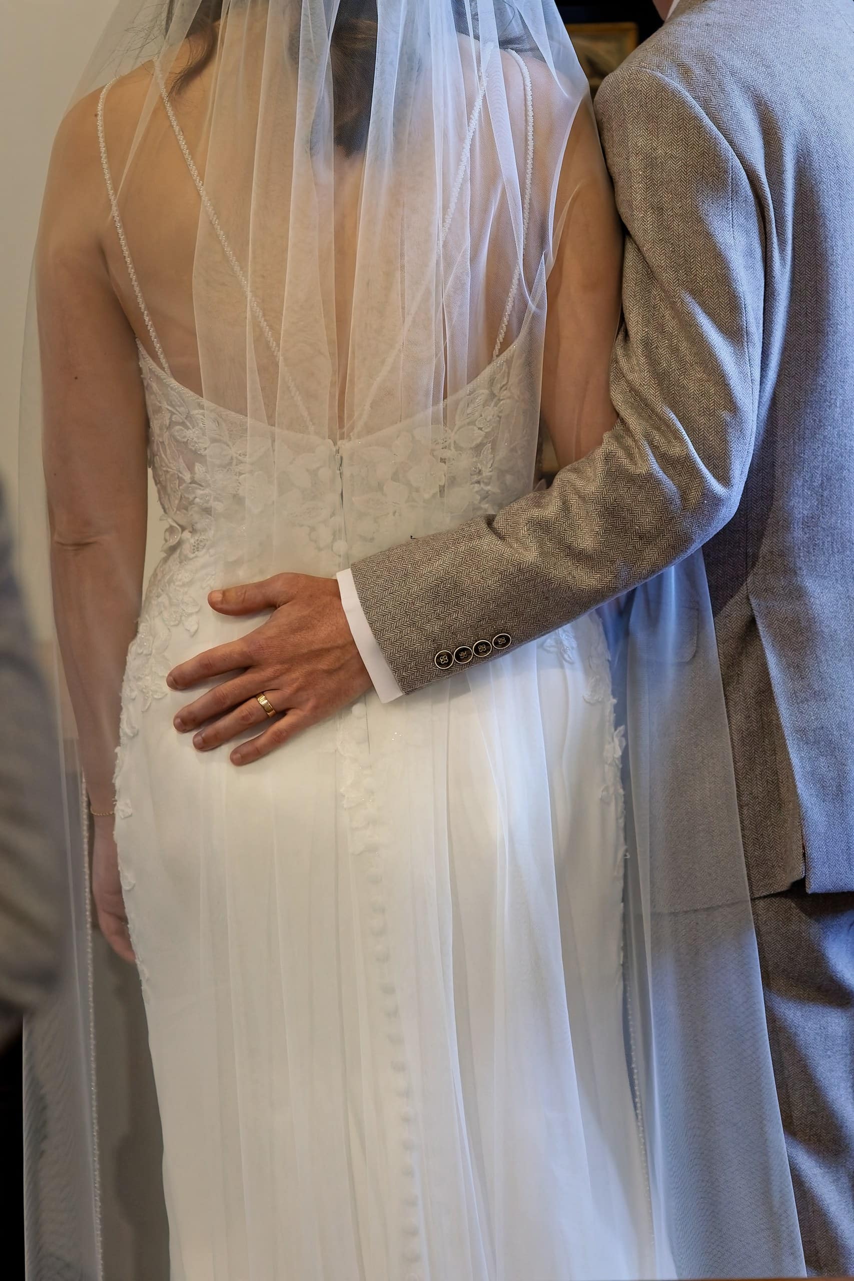 Groom with his hand on the small of the bride's back showing the lace detail of her dress
