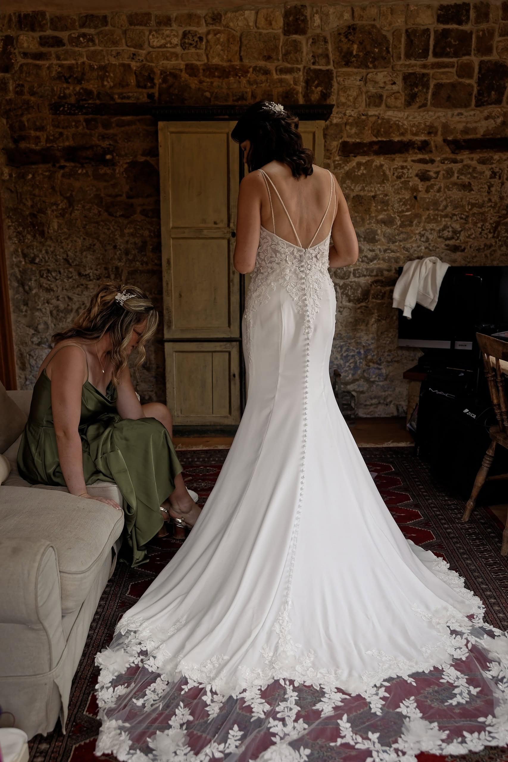 Long lace edged wedding dress train spread across the floor with the maid of honour nearby